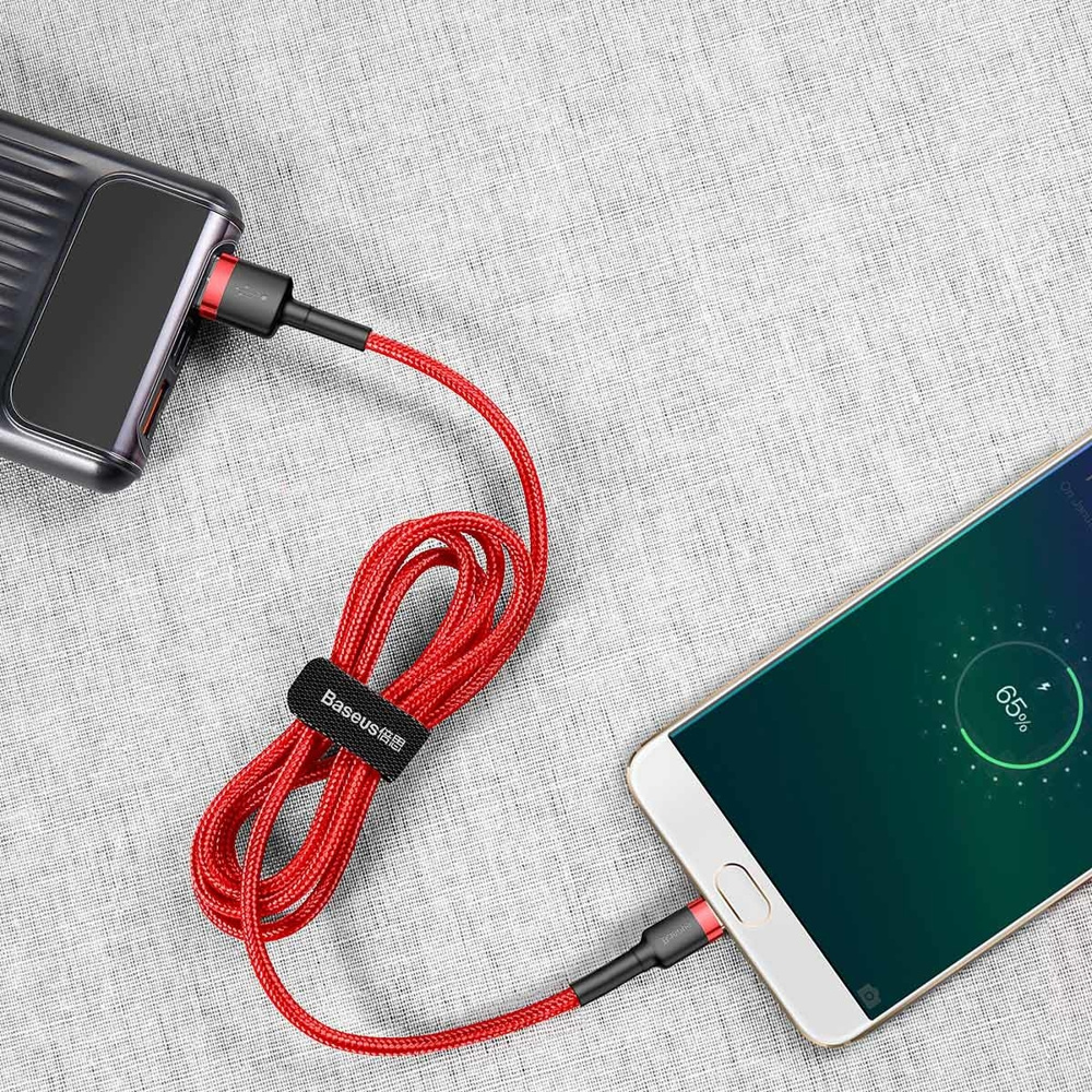 Czerwony kabel USB jest podłączony do telefonu i powerbanku. Telefon pokazuje 65% naładowania baterii.