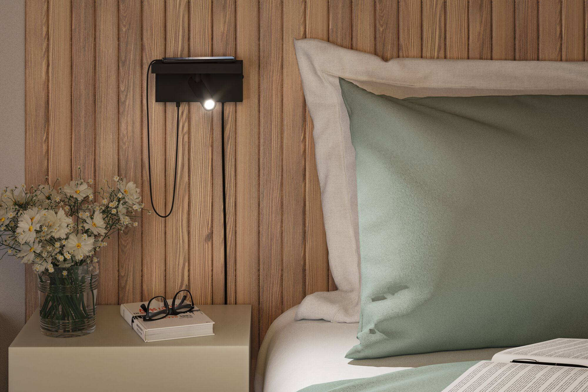 Eine Nachttischszene mit einer Wandlampe, Blumen, einem Buch mit Brille und einem teilweise sichtbaren Bett.