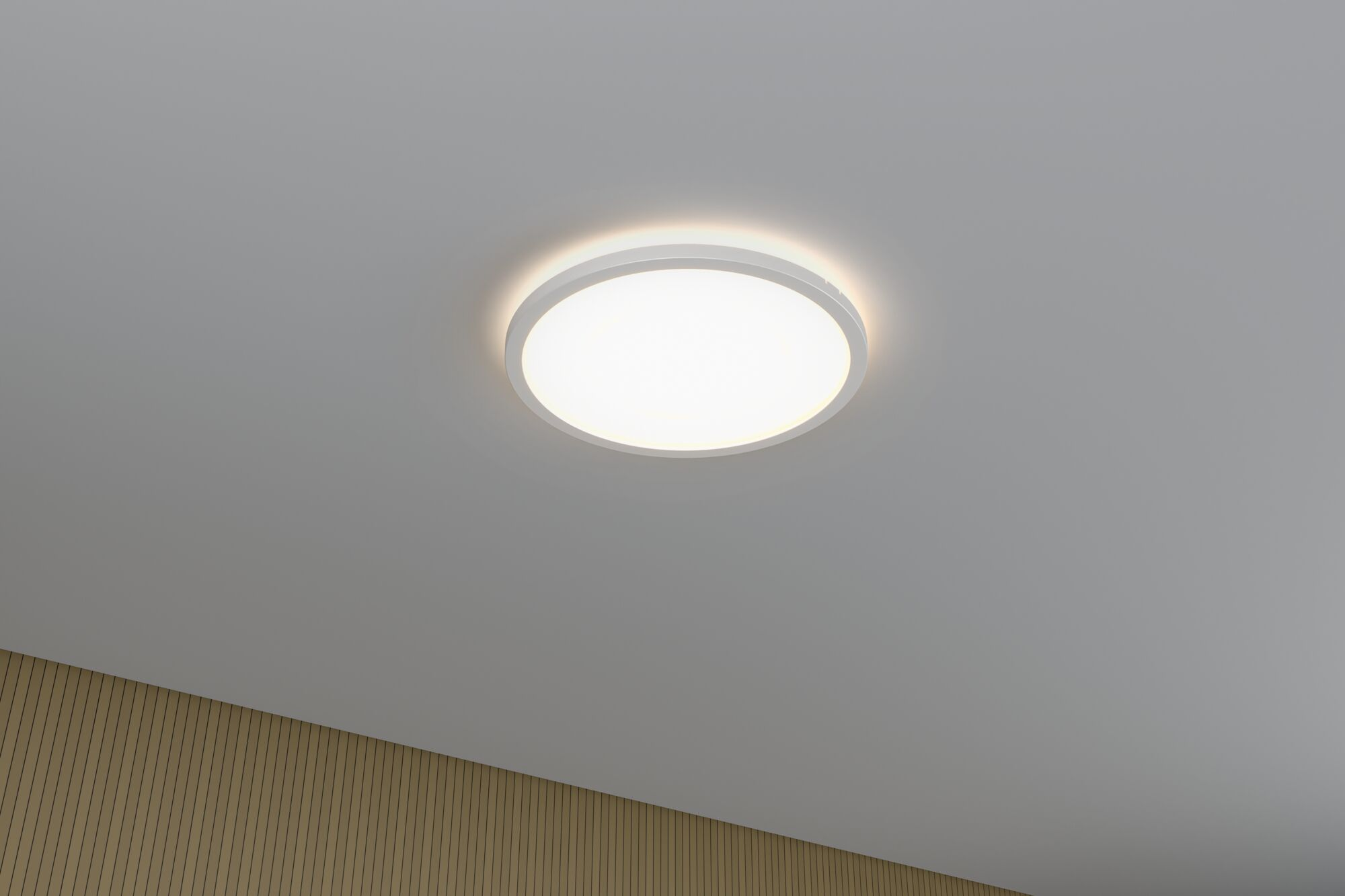 Eine runde Deckenleuchte ist an einer grauen Decke mit einer holzgetäfelten Wand darunter montiert.
