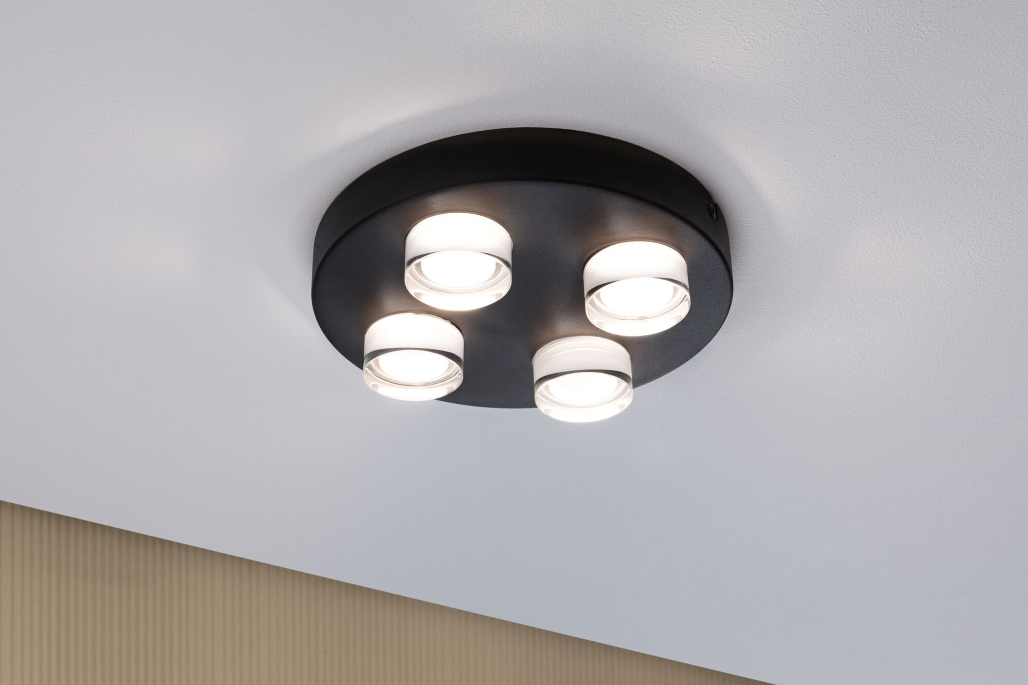 Eine schwarze Deckenleuchte verfügt über vier mattierte Glasschirme, die gleichmäßig auf einer weißen Decke verteilt sind.
