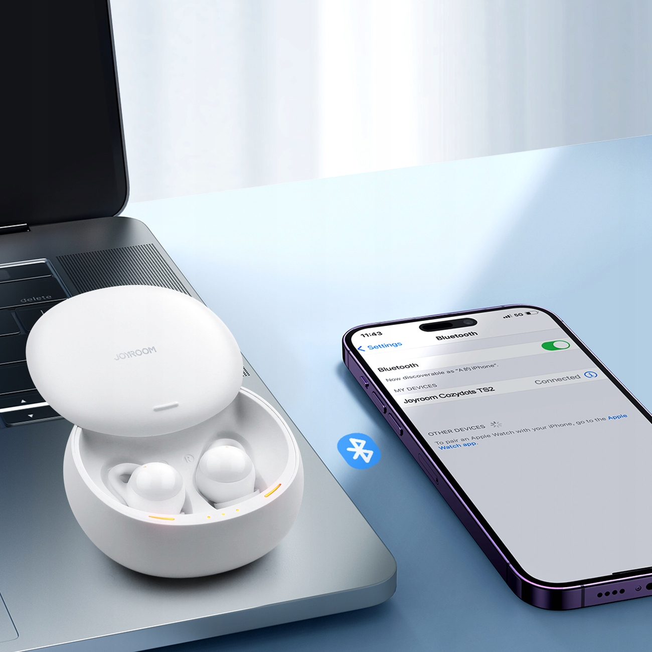 Bezprzewodowe słuchawki i smartfon leżą na laptopie, pokazując połączenie Bluetooth.