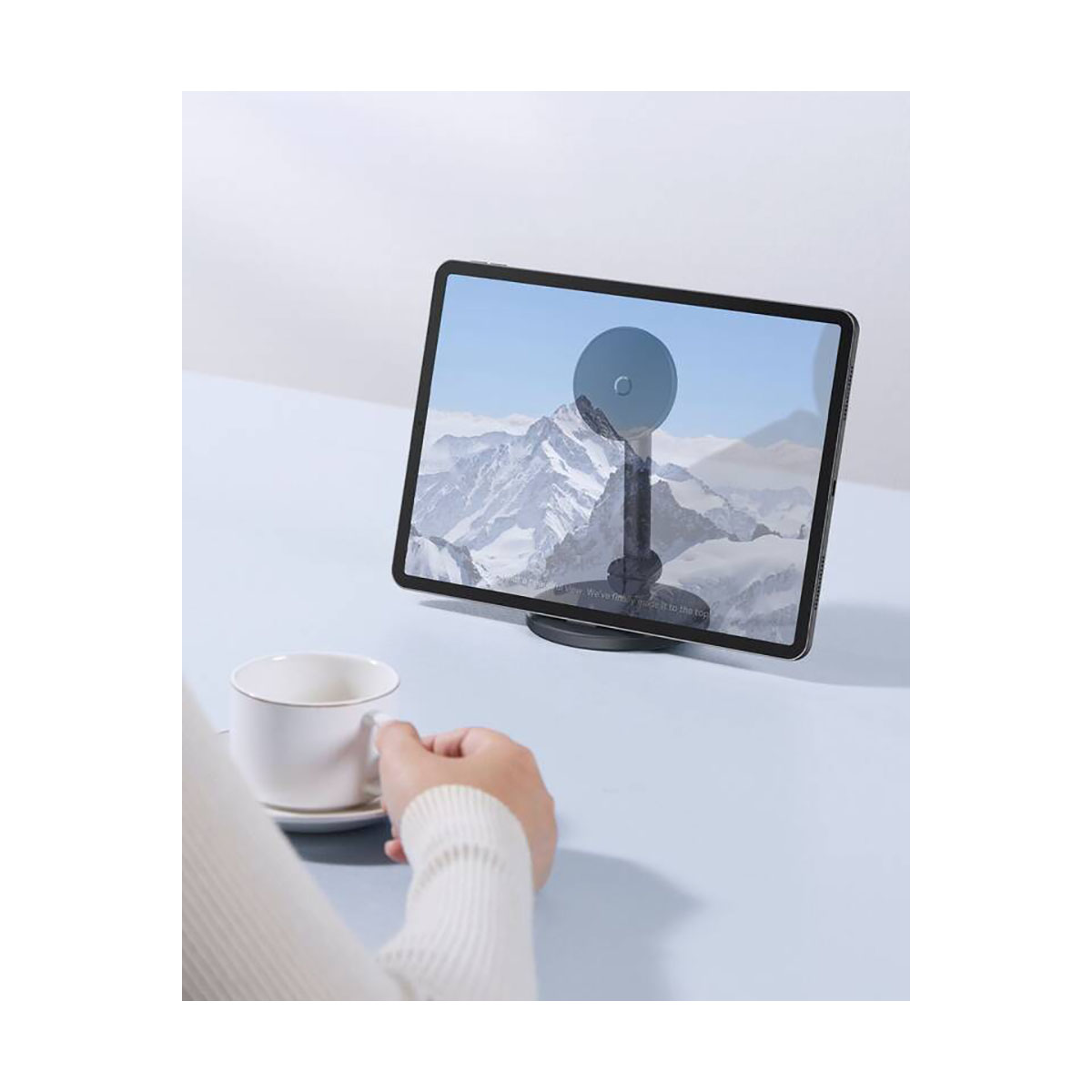 Osoba pije filiżankę kawy obok tabletu na teleskopowym wale podporowym Baseus MagPro.