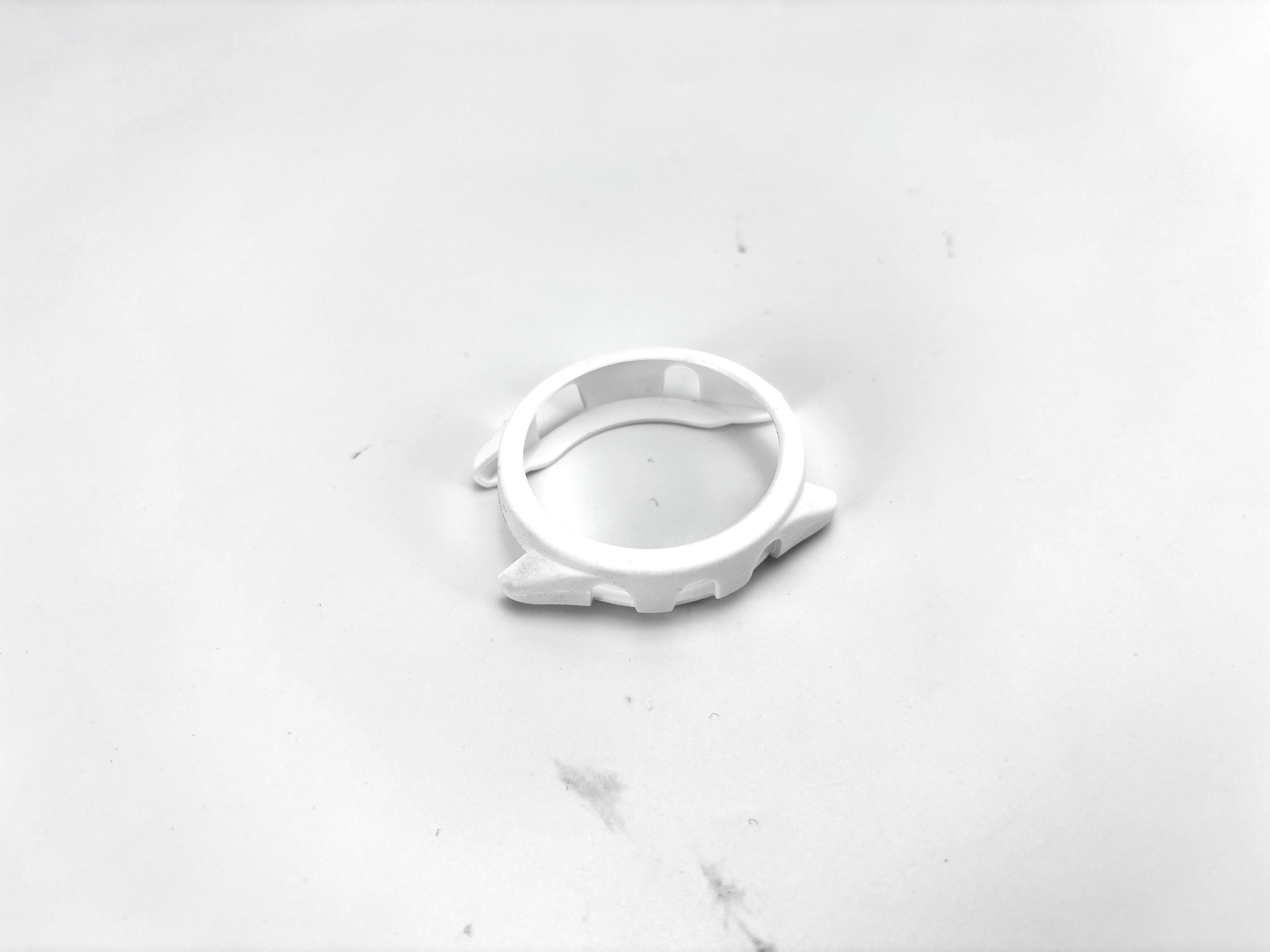 Una protezione per cassa di orologio bianca, stampata in 3D, su una superficie bianca. Ha una forma arrotondata con ritagli.