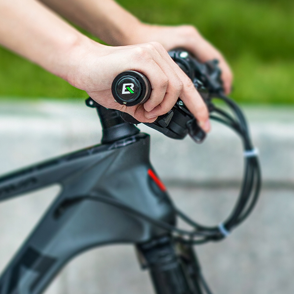 Ręce trzymają czarną kierownicę roweru z zielonym logo na końcu, na rozmytym zielonym tle.