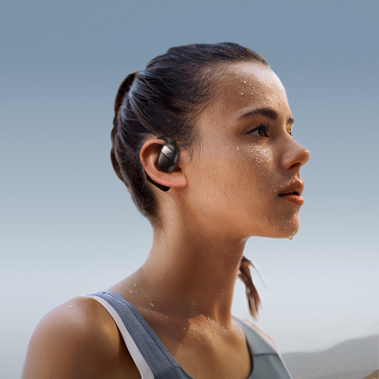 Spocona kobieta ze słuchawką w uchu na tle jasnoniebieskiego nieba.