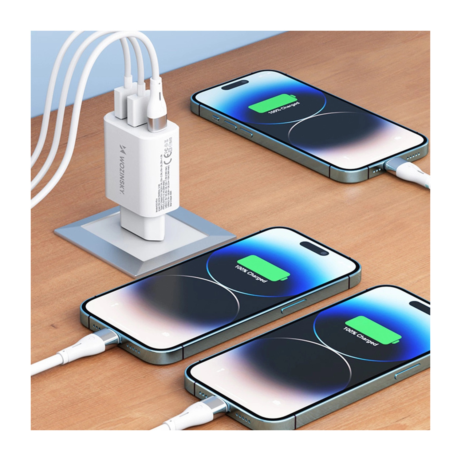 Trzy telefony podłączone do białej ładowarki na drewnianej powierzchni pokazują 100% naładowania.