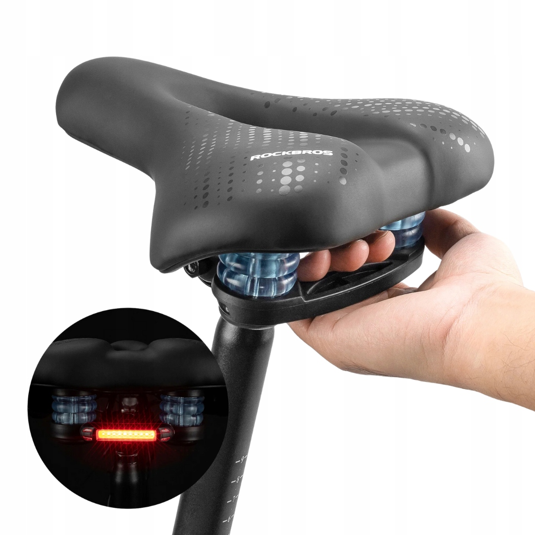 Czarne siodełko rowerowe ze światłem, trzymane przez dłoń. Tło jest białe.