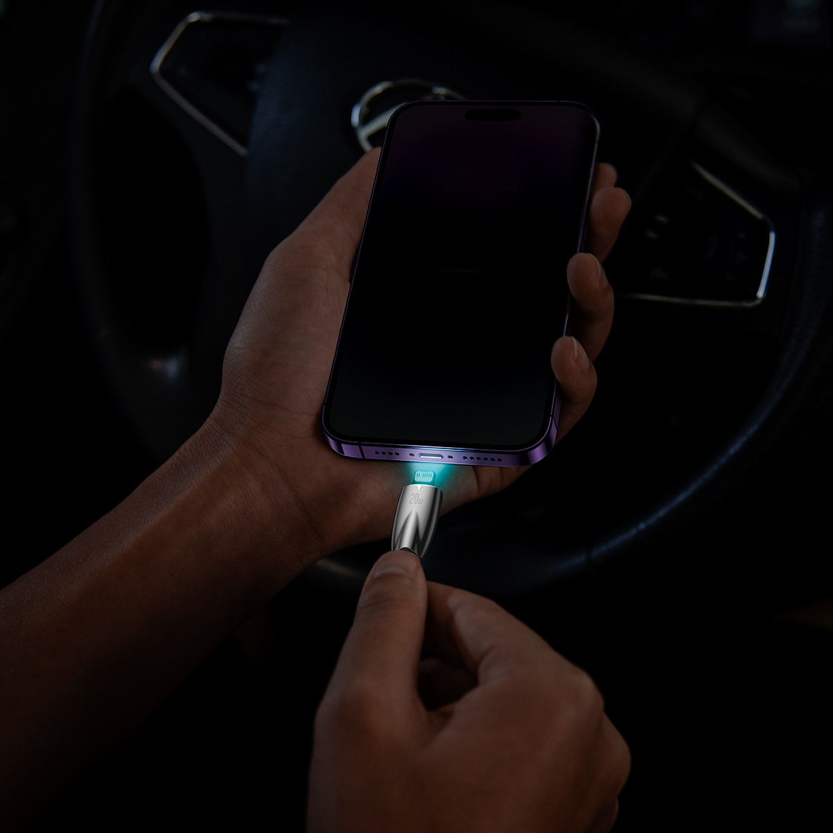 Ręka podłącza kabel ładujący Baseus do fioletowego iPhone'a w samochodzie, ze świecącym złączem.
