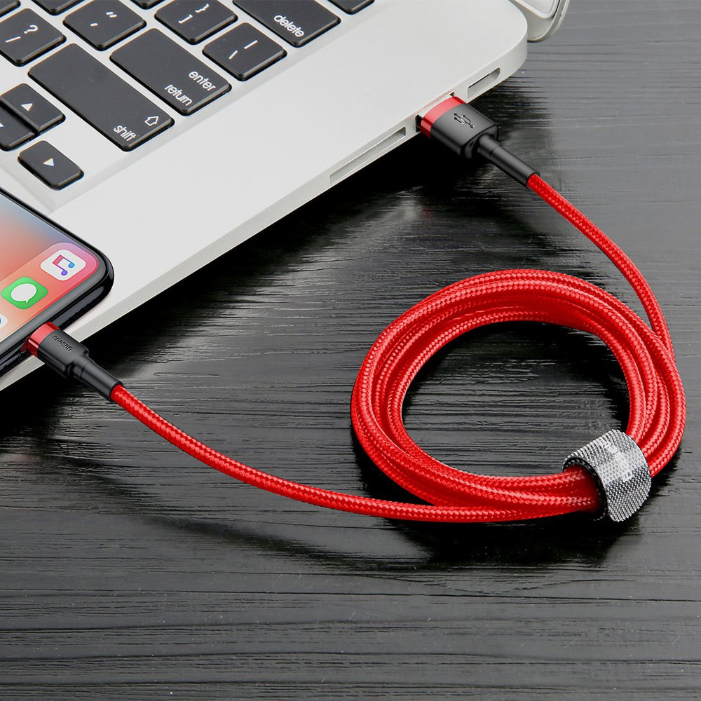 Czerwony kabel do ładowania łączy telefon z laptopem na ciemnej drewnianej powierzchni, ukazując łączność technologiczną.