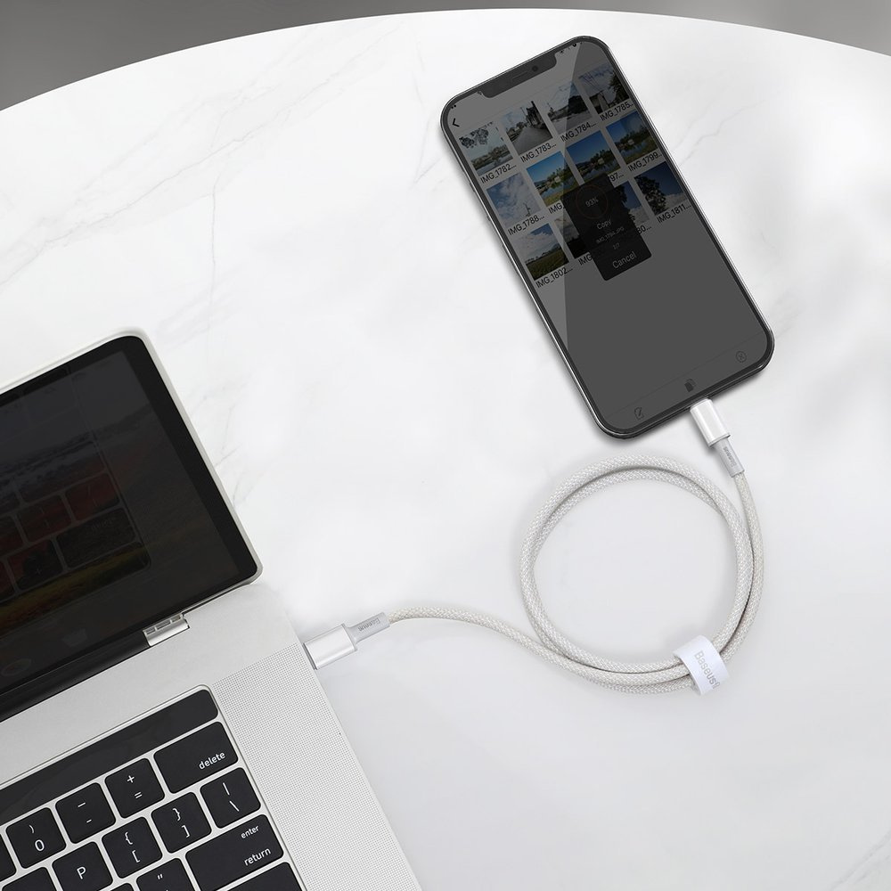 Biały kabel łączy telefon i laptop w celu przesyłania danych na marmurowej powierzchni.