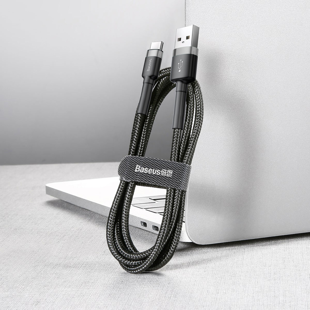 Zwarte USB-kabel met USB-C- en USB-A-connectoren, opgerold in de buurt van een laptop.