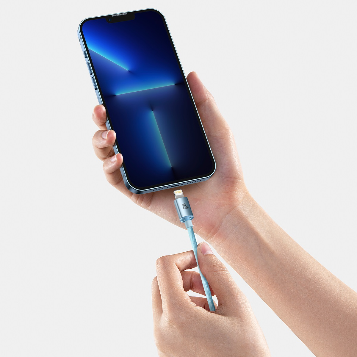 Ręce podłączają jasnoniebieski kabel Baseus do niebieskiego telefonu, ładując urządzenie.