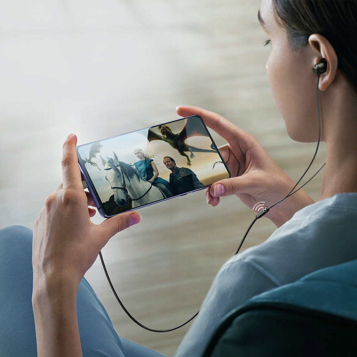 Osoba ogląda program ze smokami w telefonie, używając przewodowych słuchawek.