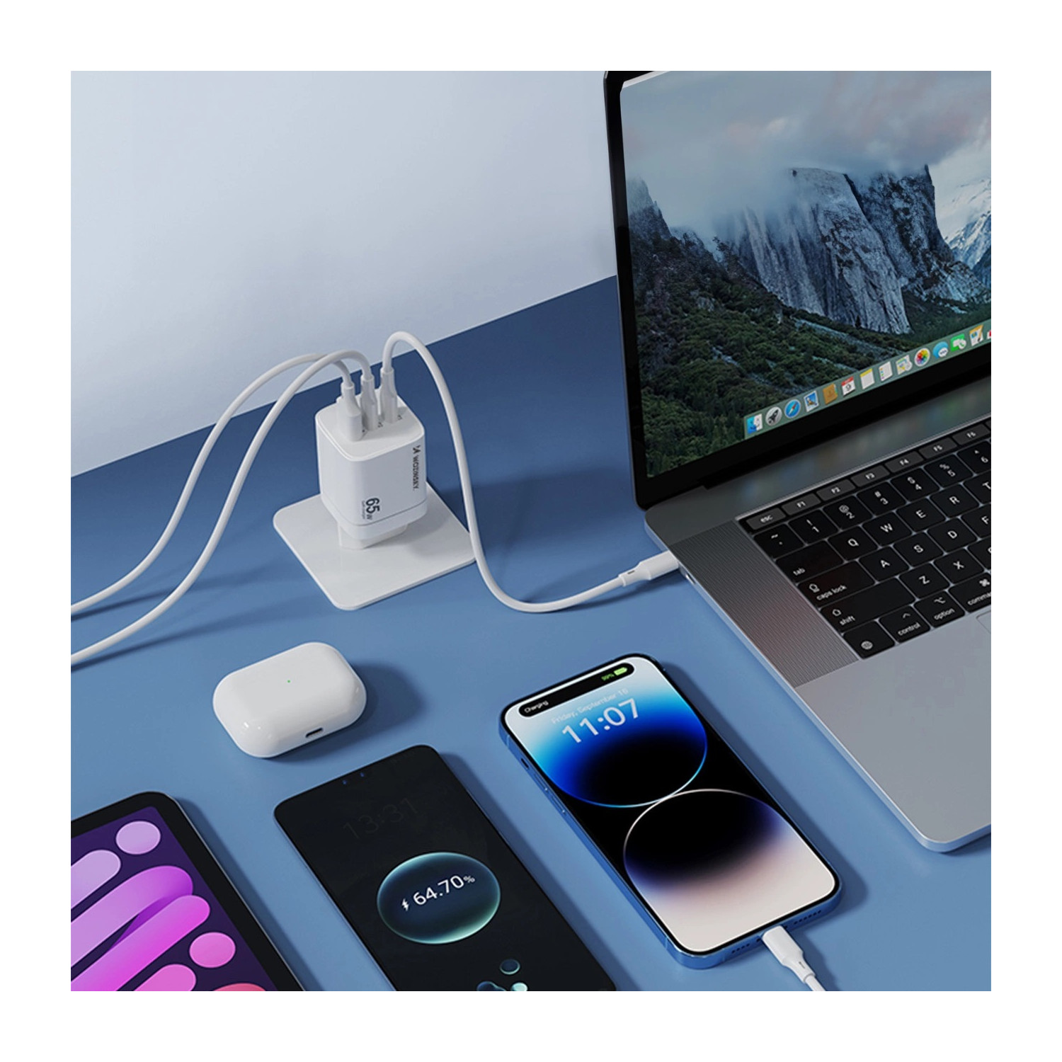 Stacja ładująca zasila urządzenia: laptop, dwa telefony i słuchawki douszne na niebieskiej powierzchni.