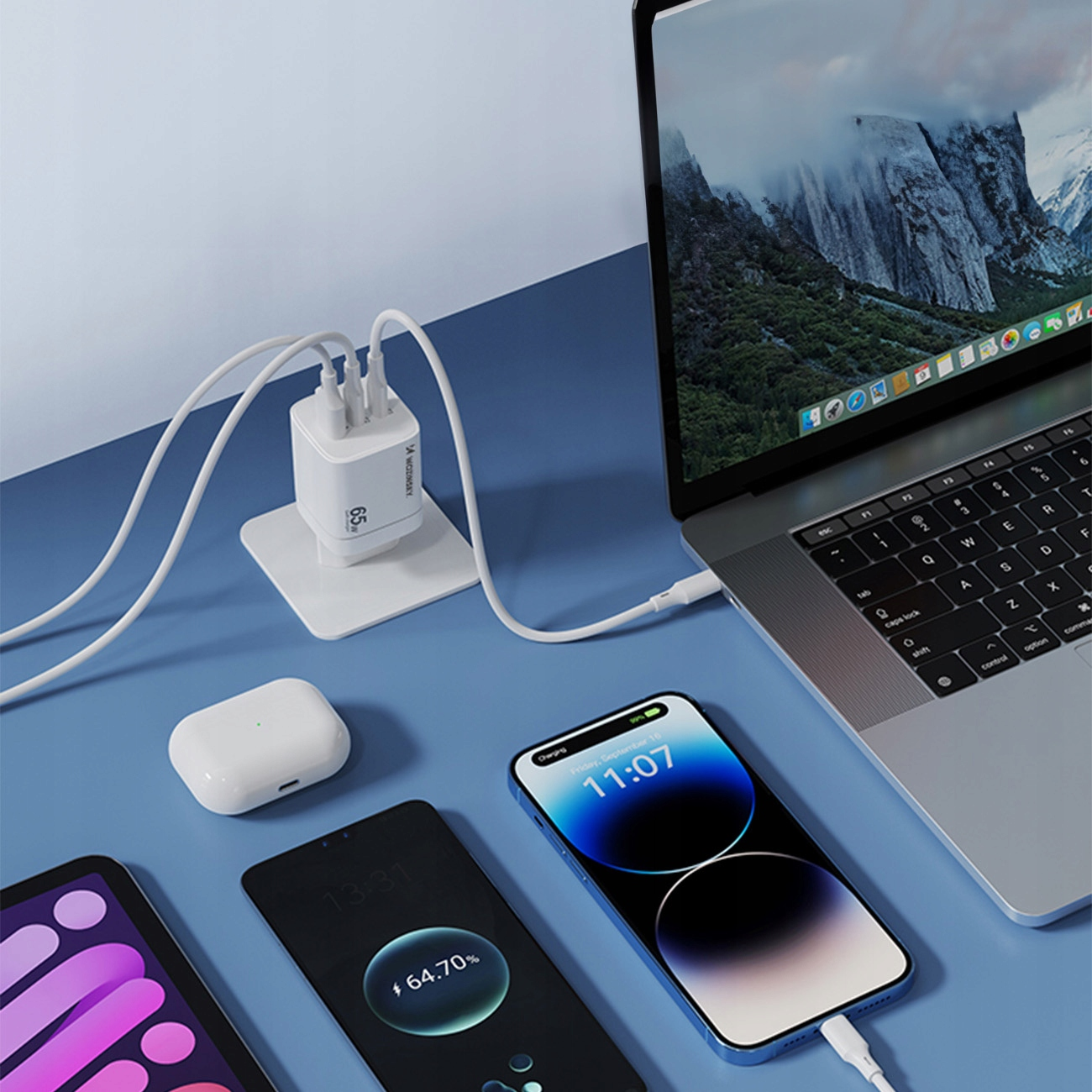 Stacja ładująca z laptopem, telefonami i słuchawkami na niebieskiej powierzchni.