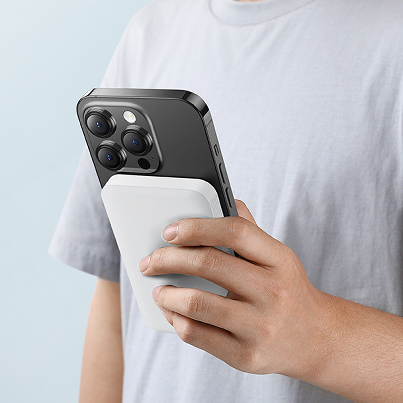 Ręka trzyma telefon przymocowany do białego magnetycznego power banku Baseus.