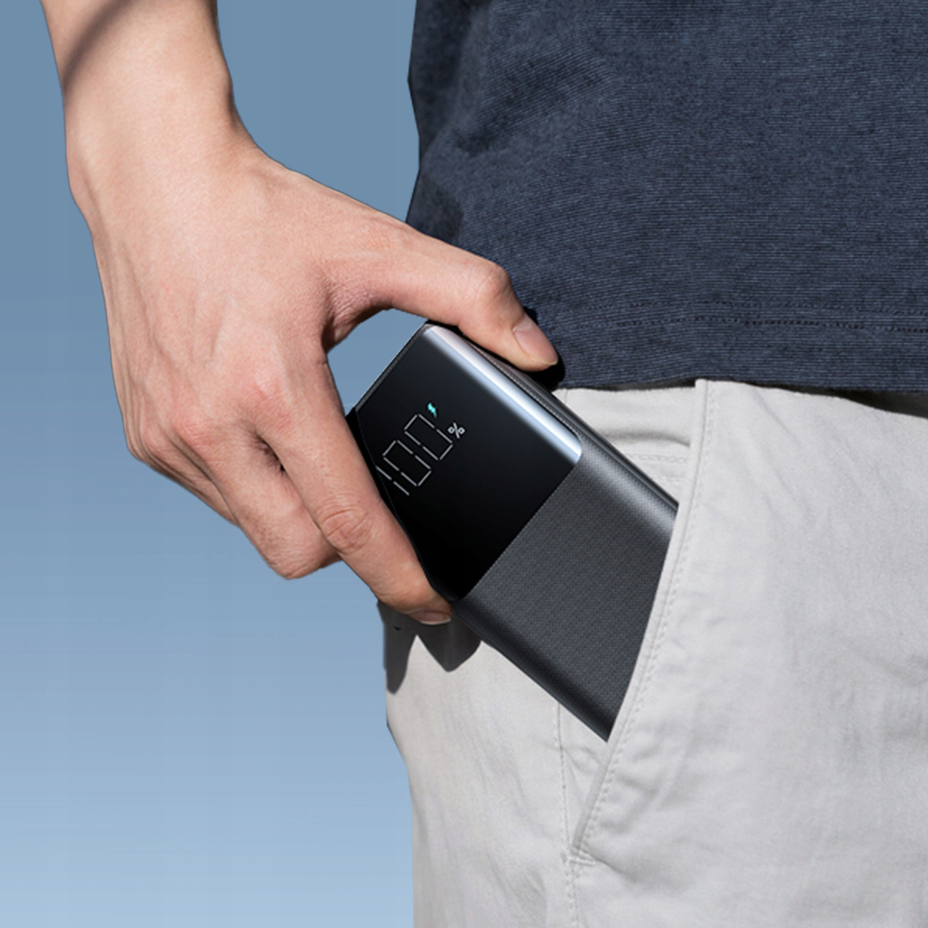 Obraz przedstawia dłoń wkładającą power bank do jasnej kieszeni.