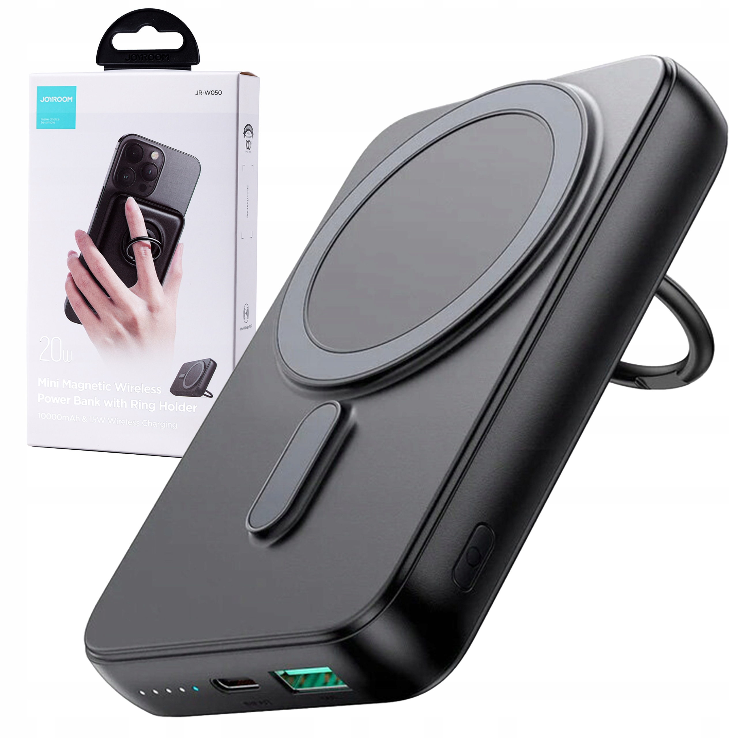 Czarny power bank z uchwytem na pierścień, pudełko w tle. Jest czarny i szary. Ręka trzyma telefon.