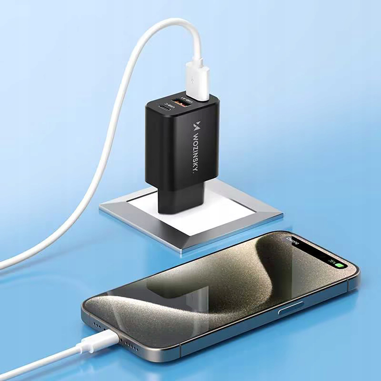 Czarna ładowarka Wozinsky podłączona do telefonu na niebieskiej powierzchni.