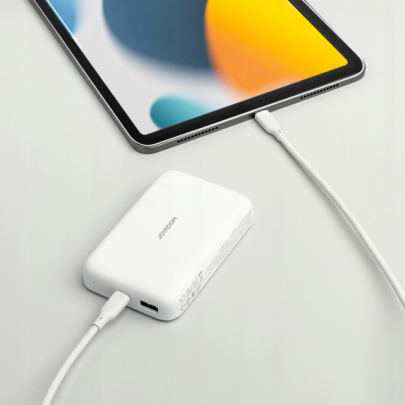 Biały power bank ładujący tablet. Biały kabel łączący. Białe tło.