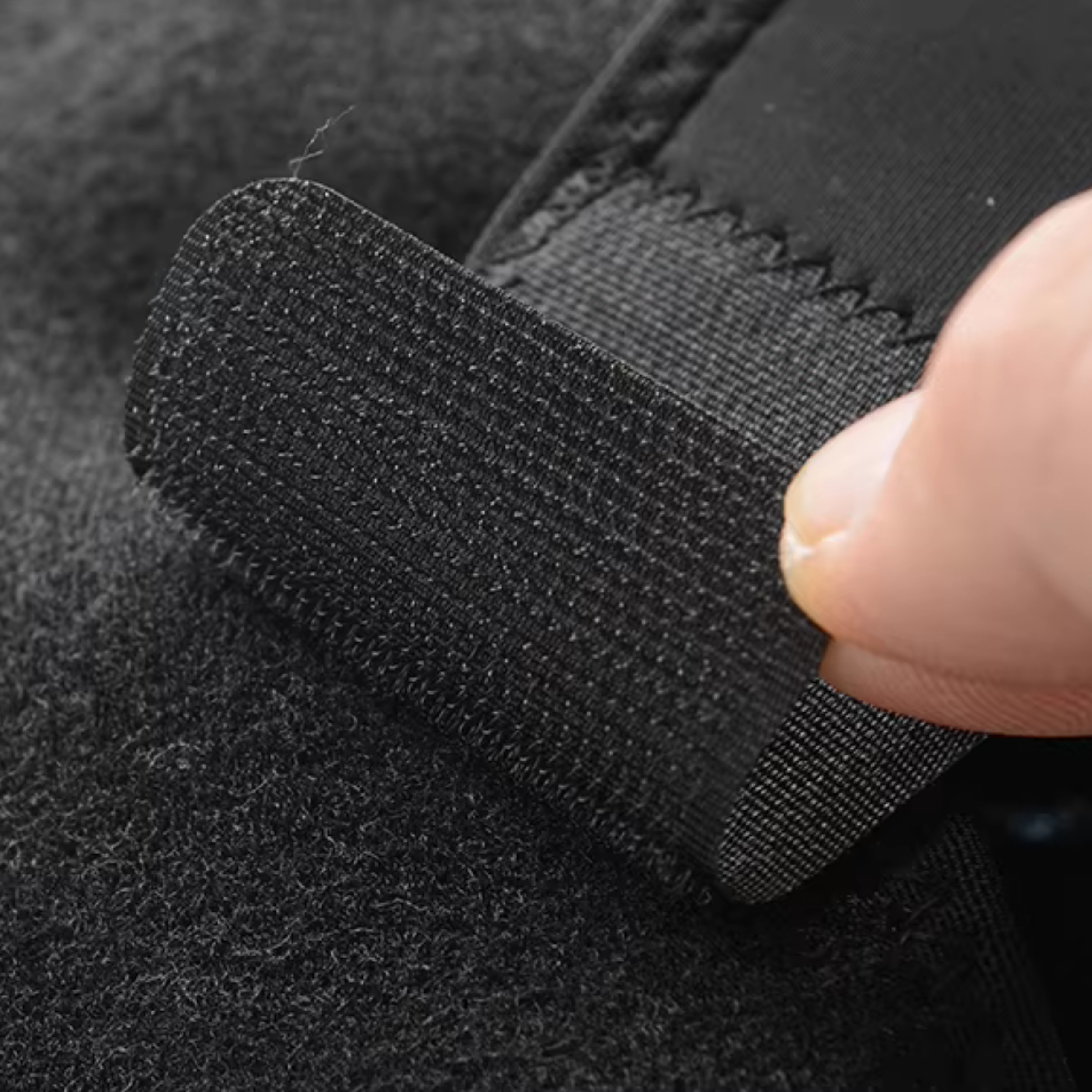 Zbliżenie pokazuje palec odciągający czarny elastyczny pasek, odsłaniając jego teksturowaną spodnią stronę na ciemnym tle.