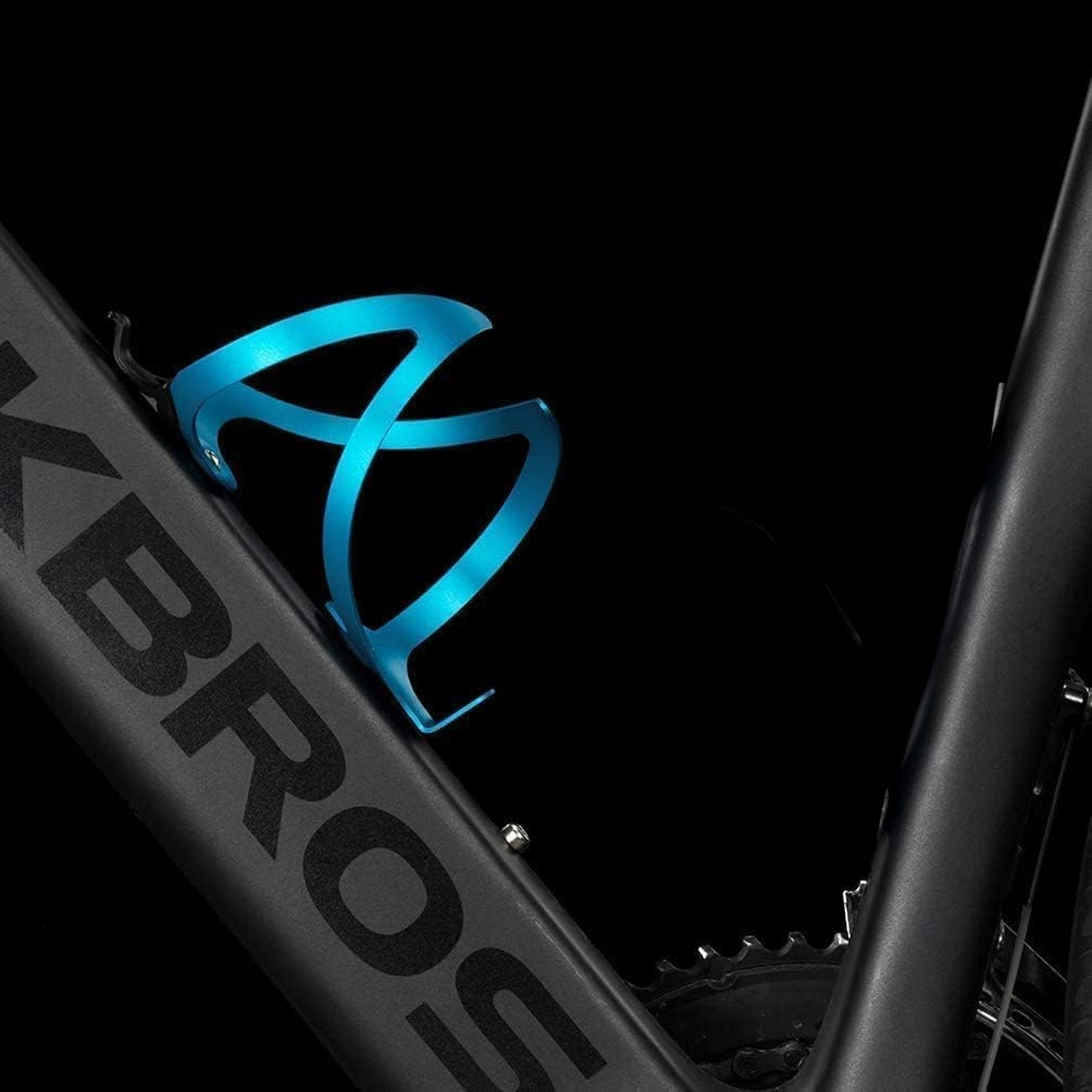 Niebieski koszyk na bidon rowerowy jest zamontowany na czarnej ramie, na ciemnym tle.