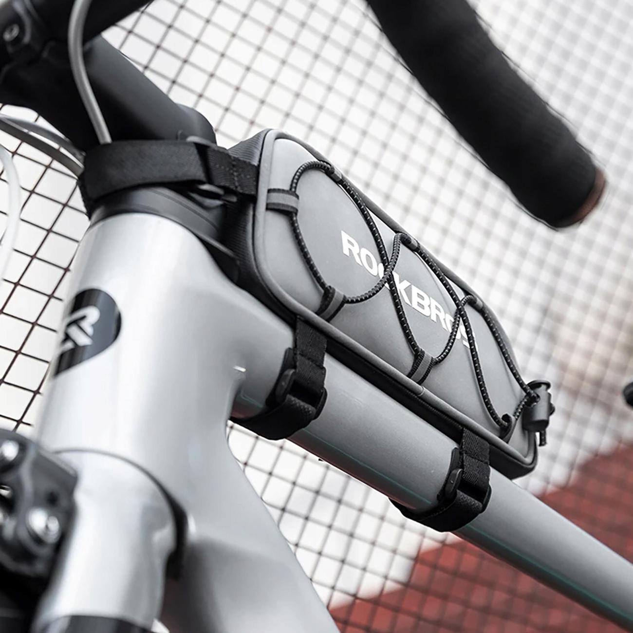 Szara torba rowerowa jest zamontowana na ramie, z widocznym słowem „ROCKBROS”, z siatką drucianą w tle.