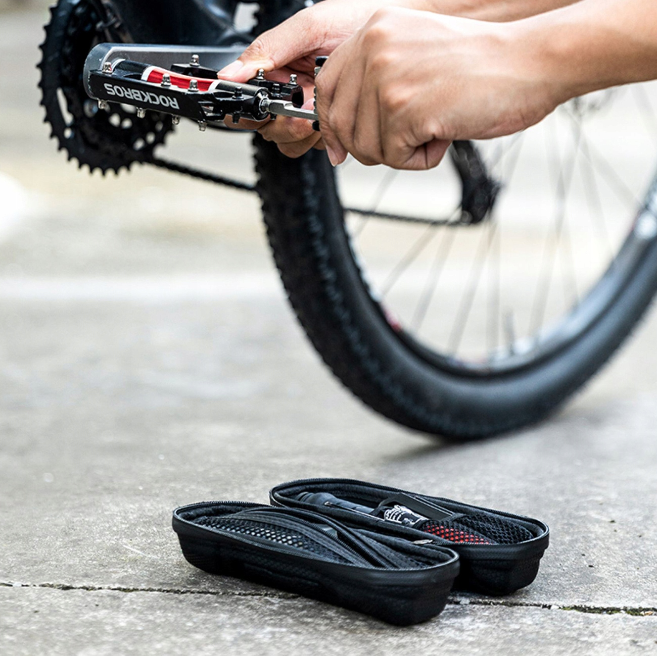 Osoba używa narzędzia ROCKBROS do naprawy roweru, z czarnym futerałem na narzędzia na ziemi.
