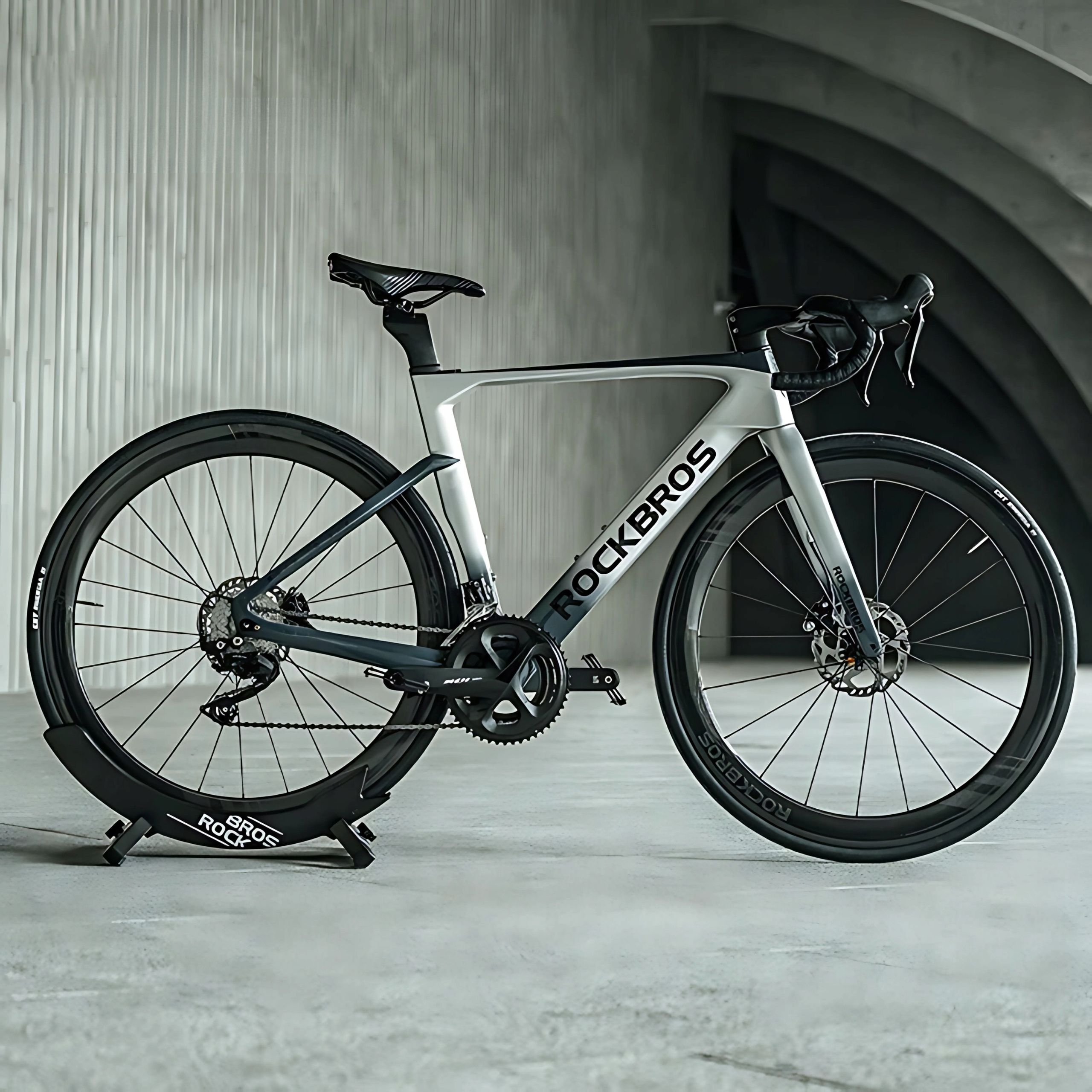 Szaro-czarny rower szosowy firmy Rockbros jest ustawiony na pasującym stojaku rowerowym w studio.