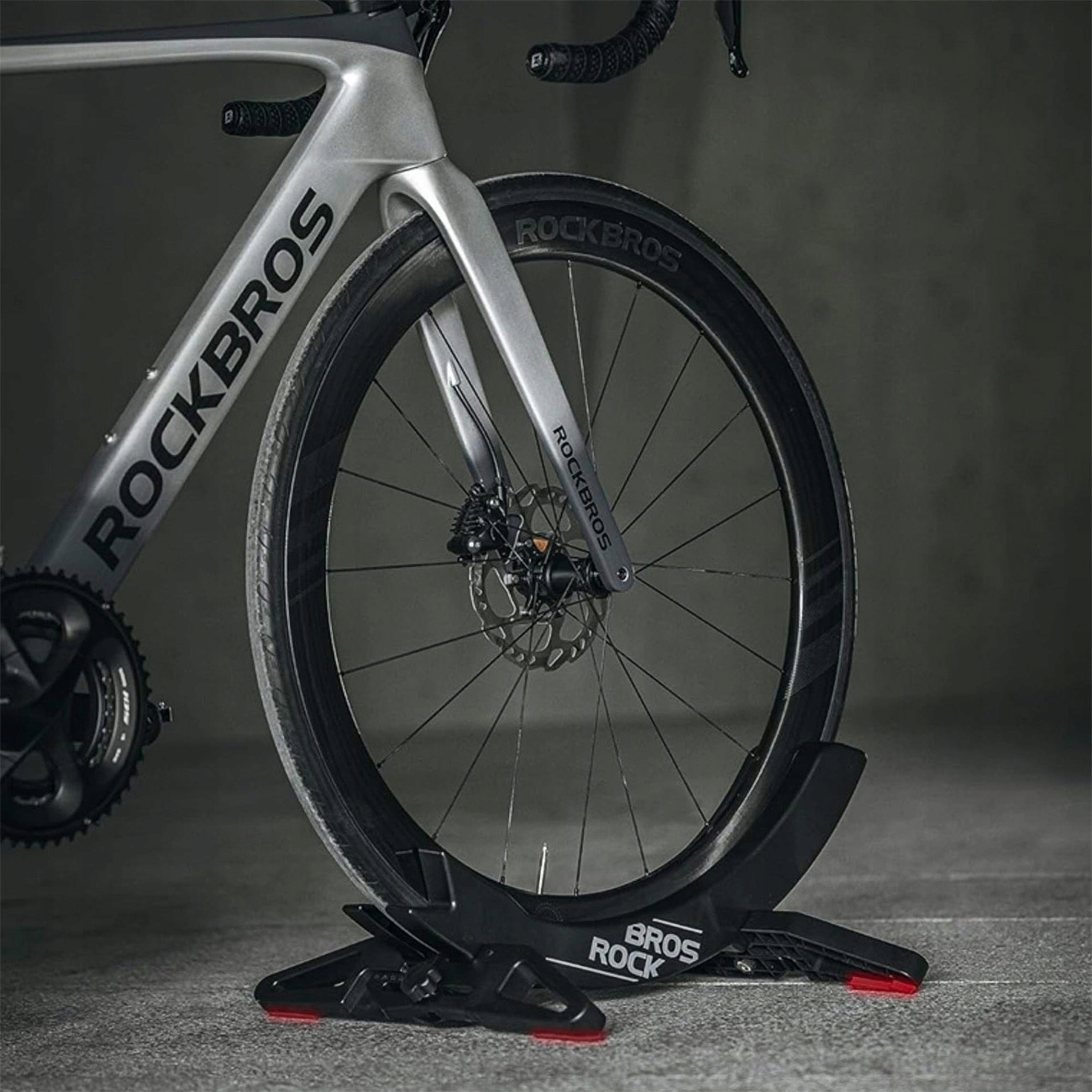 Szary rower szosowy Rockbros jest zabezpieczony na czarnym stojaku rowerowym Bros Rock.
