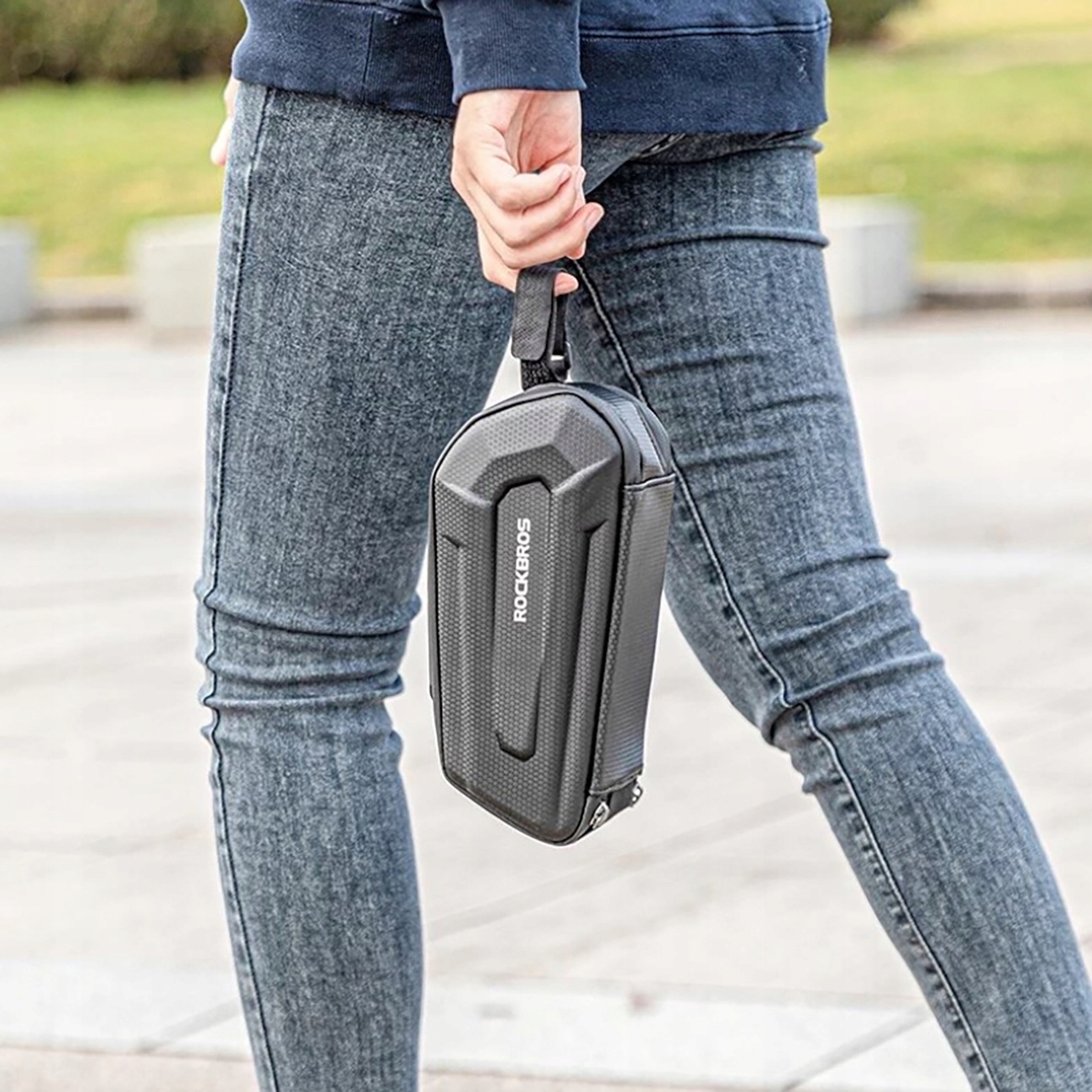 Kobieta trzyma czarną torbę rowerową ROCKBROS, prezentując jej kompaktową konstrukcję i pasek do noszenia.