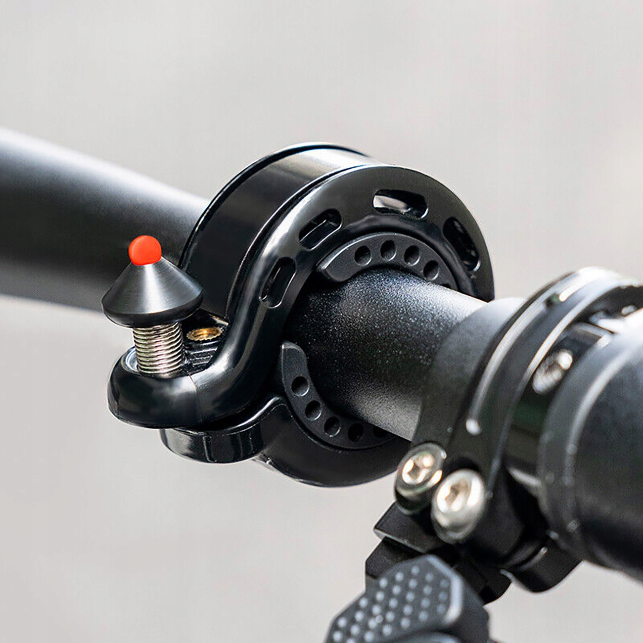 Zbliżenie czarnego dzwonka rowerowego z czerwonym młoteczkiem zamontowanym na kierownicy.