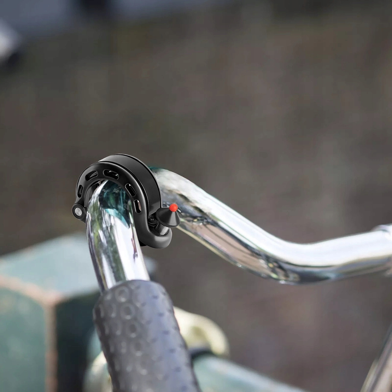 Czarny dzwonek rowerowy jest zamontowany na srebrnej kierownicy roweru, na rozmytym tle.