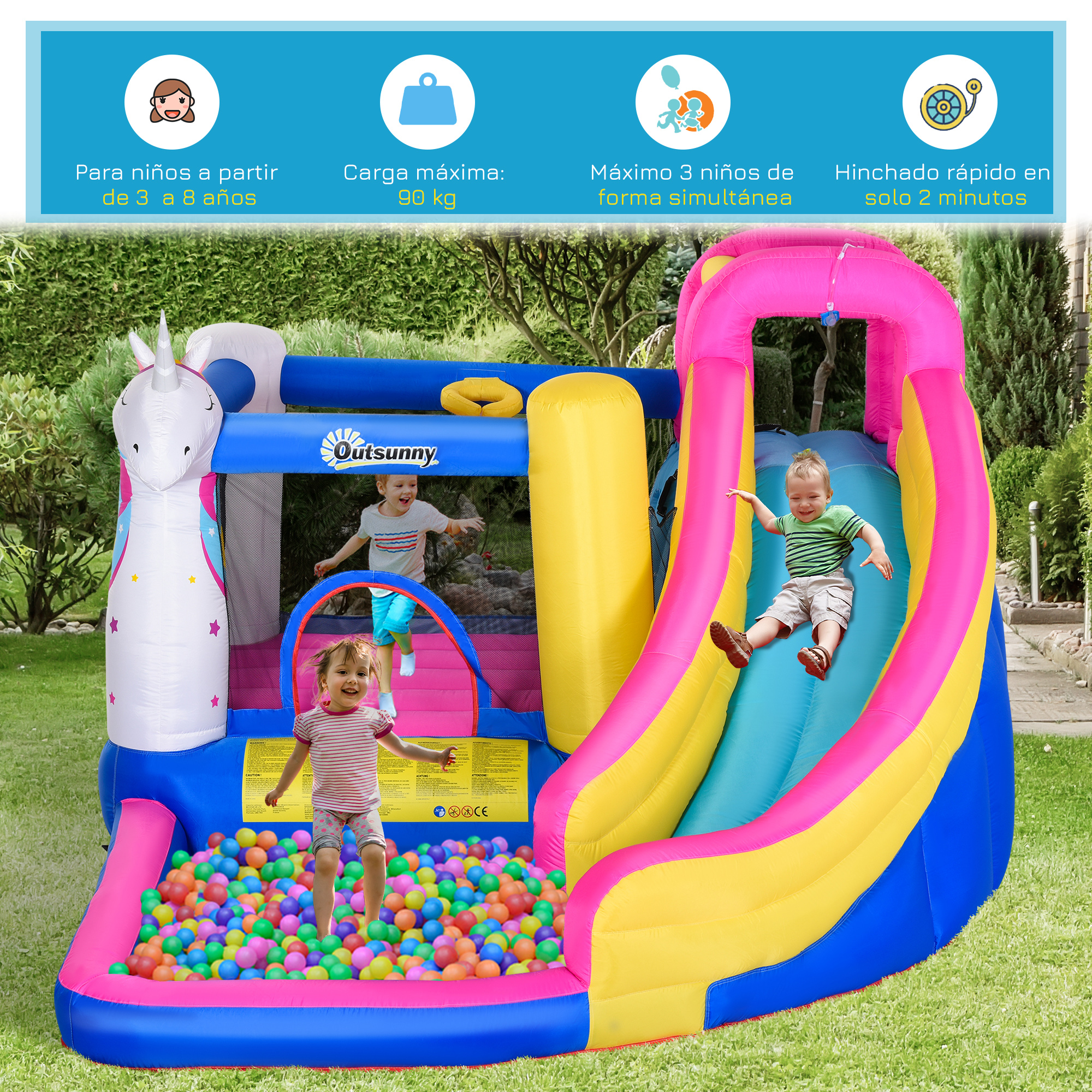 Niños jugando en un colorido castillo hinchable con tobogán y piscina de bolas sobre césped verde.