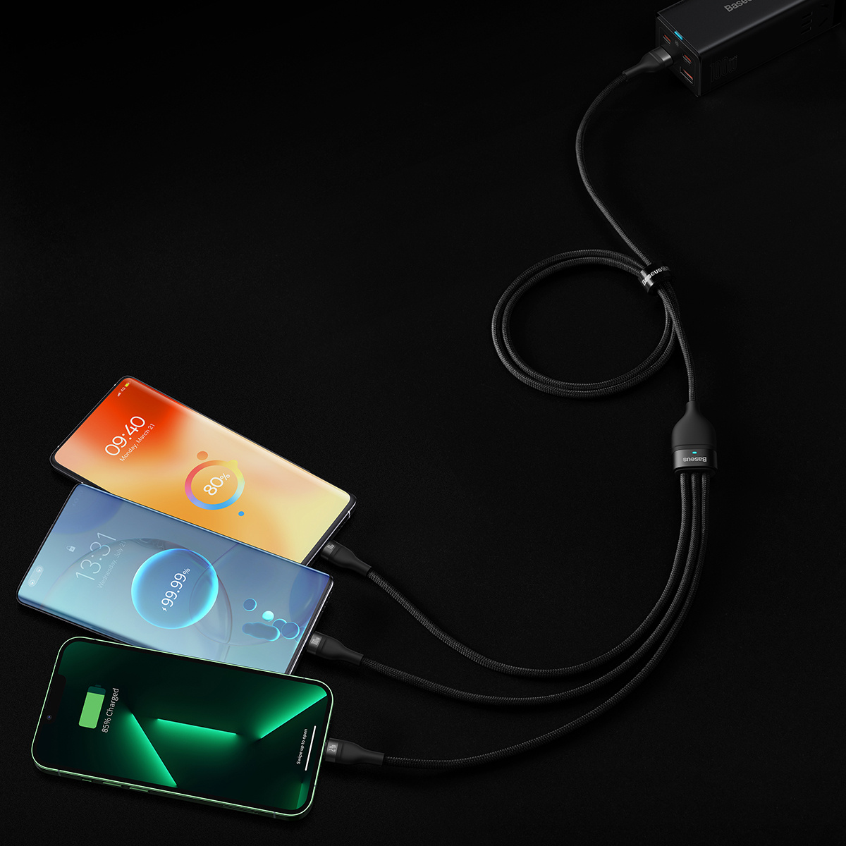 Tre smartphone si stanno caricando contemporaneamente con un cavo multi-connettore su una superficie nera, alimentati da un caricabatterie Baseus.