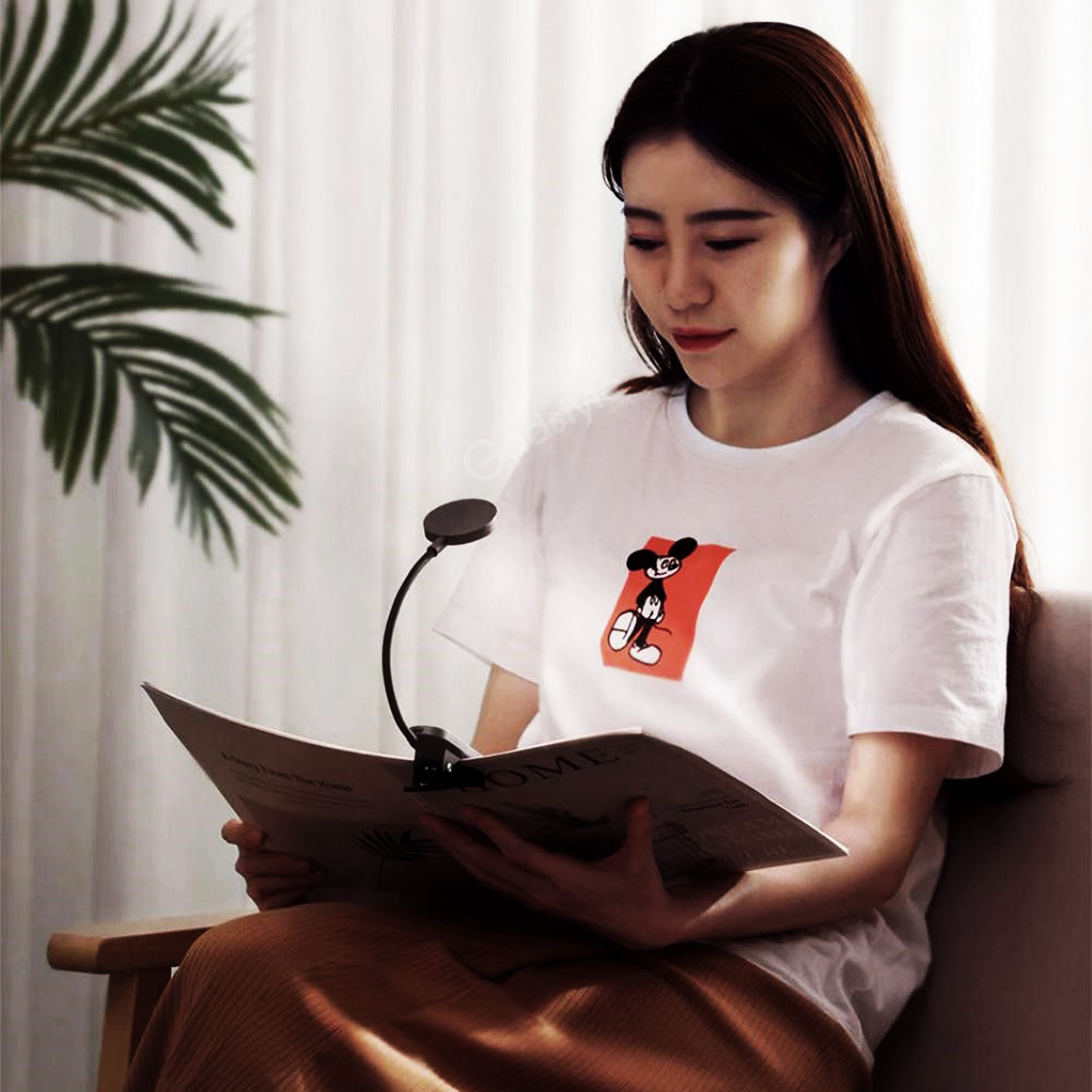 Kobieta czyta książkę z lampką na klips. Ma na sobie białą koszulkę z kreskówką.