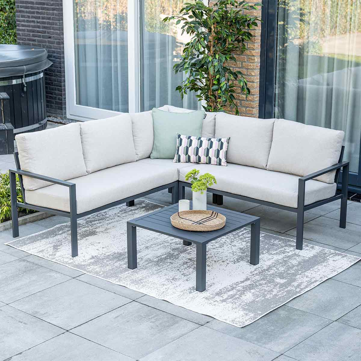 Gray sectional sofa with cushions and a square table on a patio with a patterned rug.