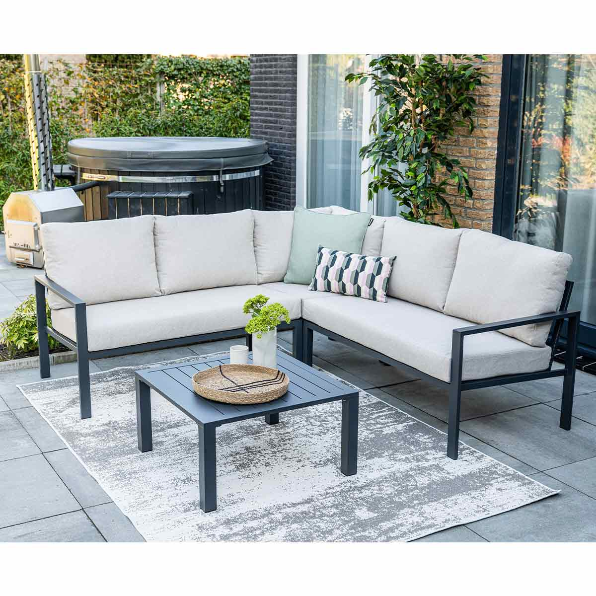 Gray sectional sofa with cushions and a square table on a patio with a patterned rug.