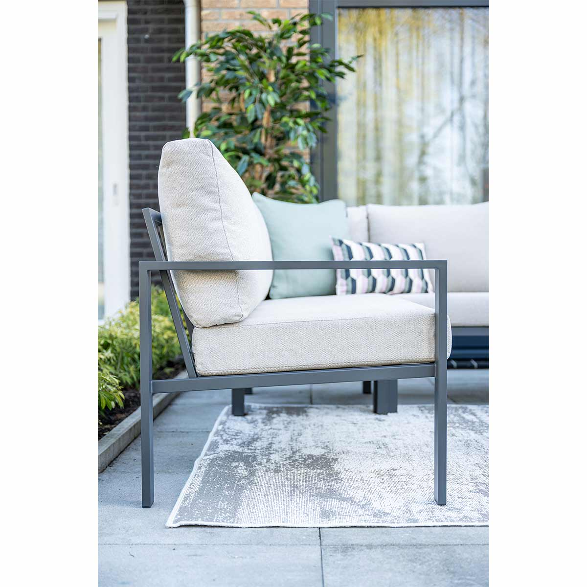 Gray chair with a cushion and a sectional sofa on a patio with a patterned rug.