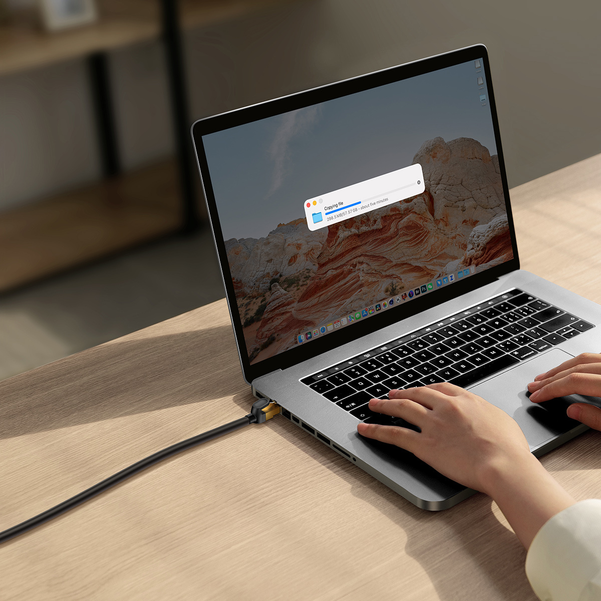 Laptop na drewnianym biurku, podłączony do czarnego kabla Ethernet.