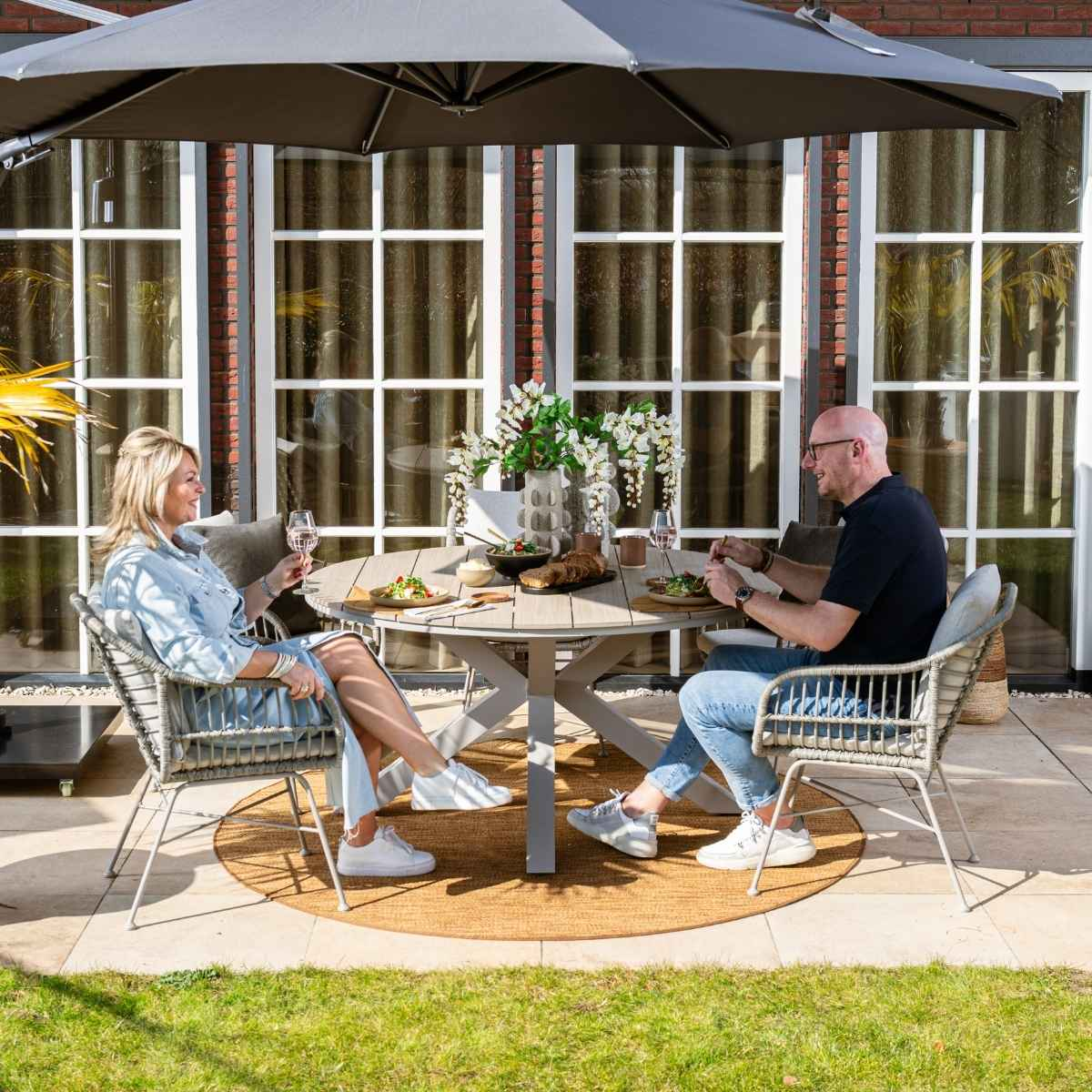 Two people sitting at an outdoor dining table under an umbrella. Food and drinks are present.