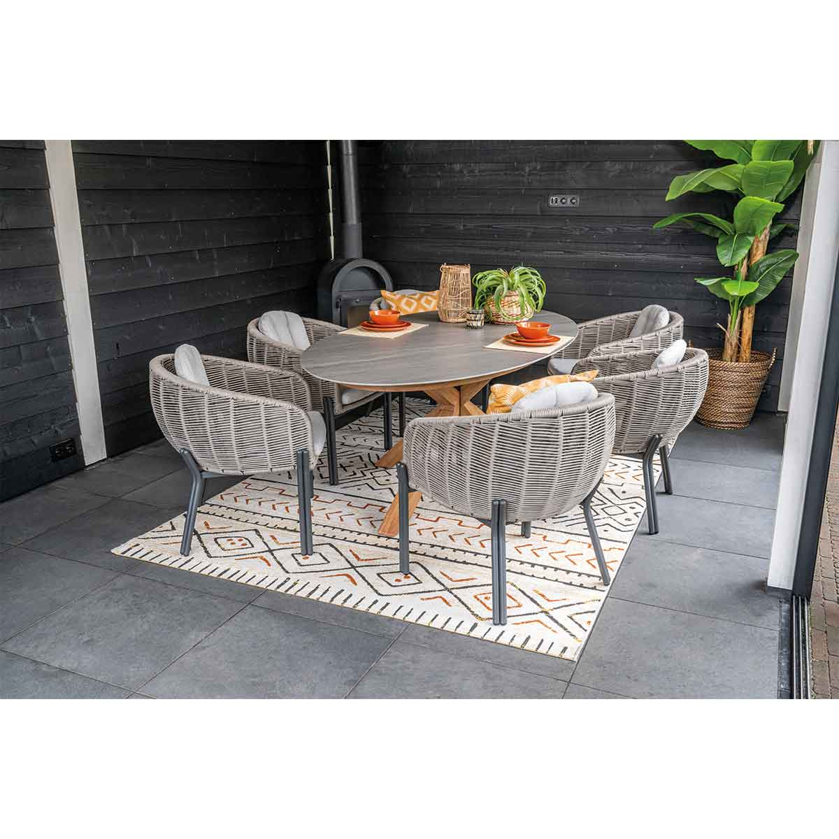 Outdoor dining area with a round table, six woven chairs, and a patterned rug.