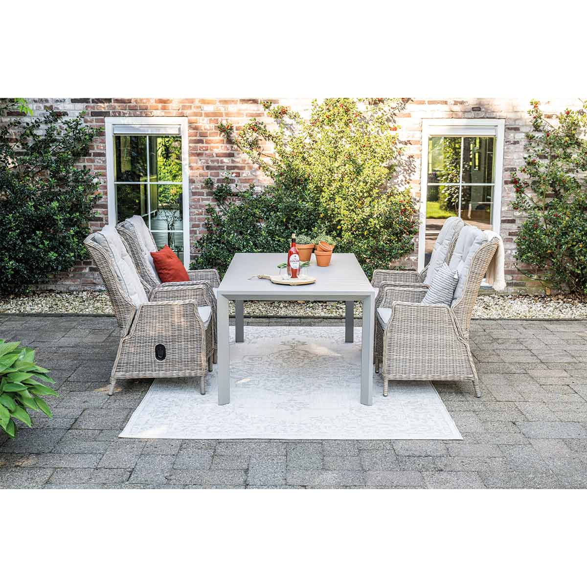 Eetset voor buiten op een terras met een grijze tafel, zes geweven stoelen en een wit vloerkleed.