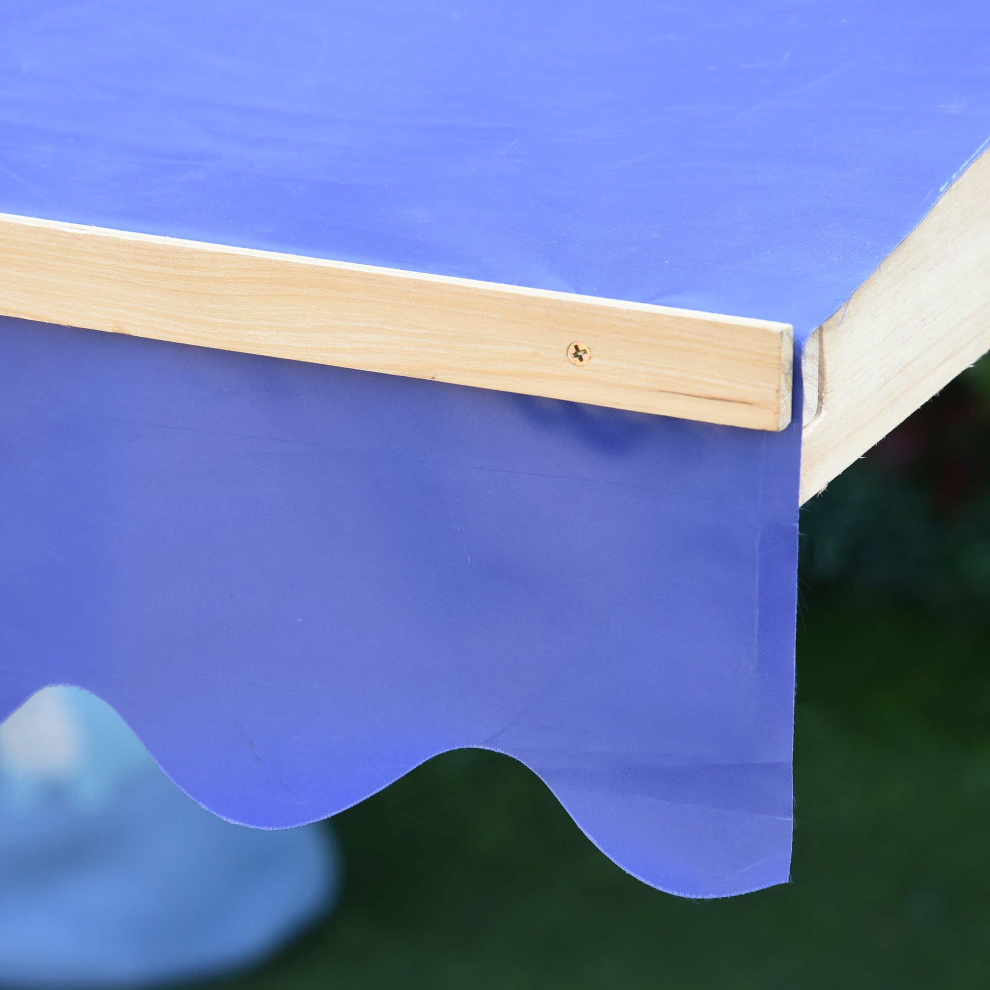 Un primer plano muestra el toldo de poliéster azul sujeto al marco de madera de un arenero.