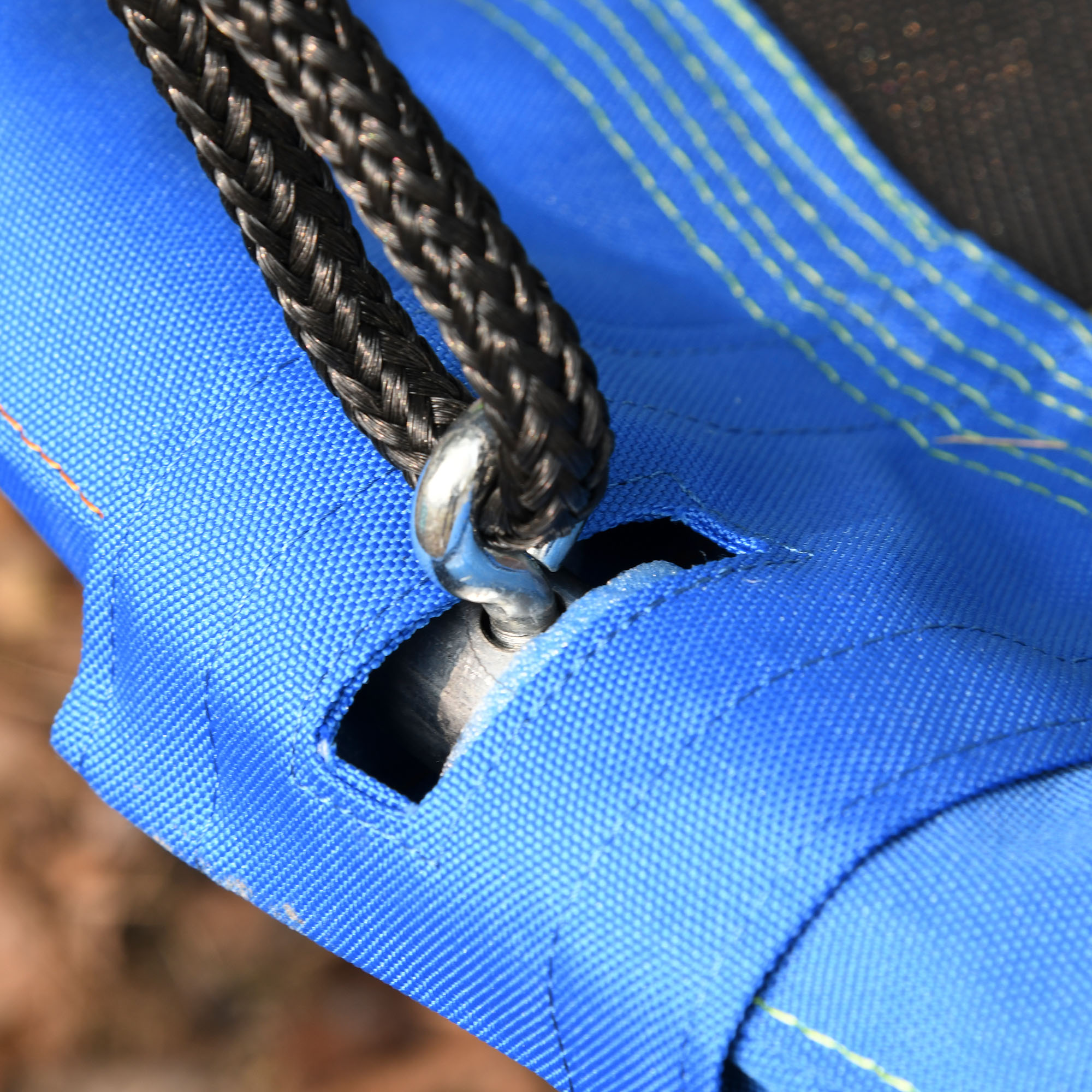 Primer plano de un detalle de columpio azul que muestra cuerda negra trenzada, anillo de metal y construcción de tela resistente.