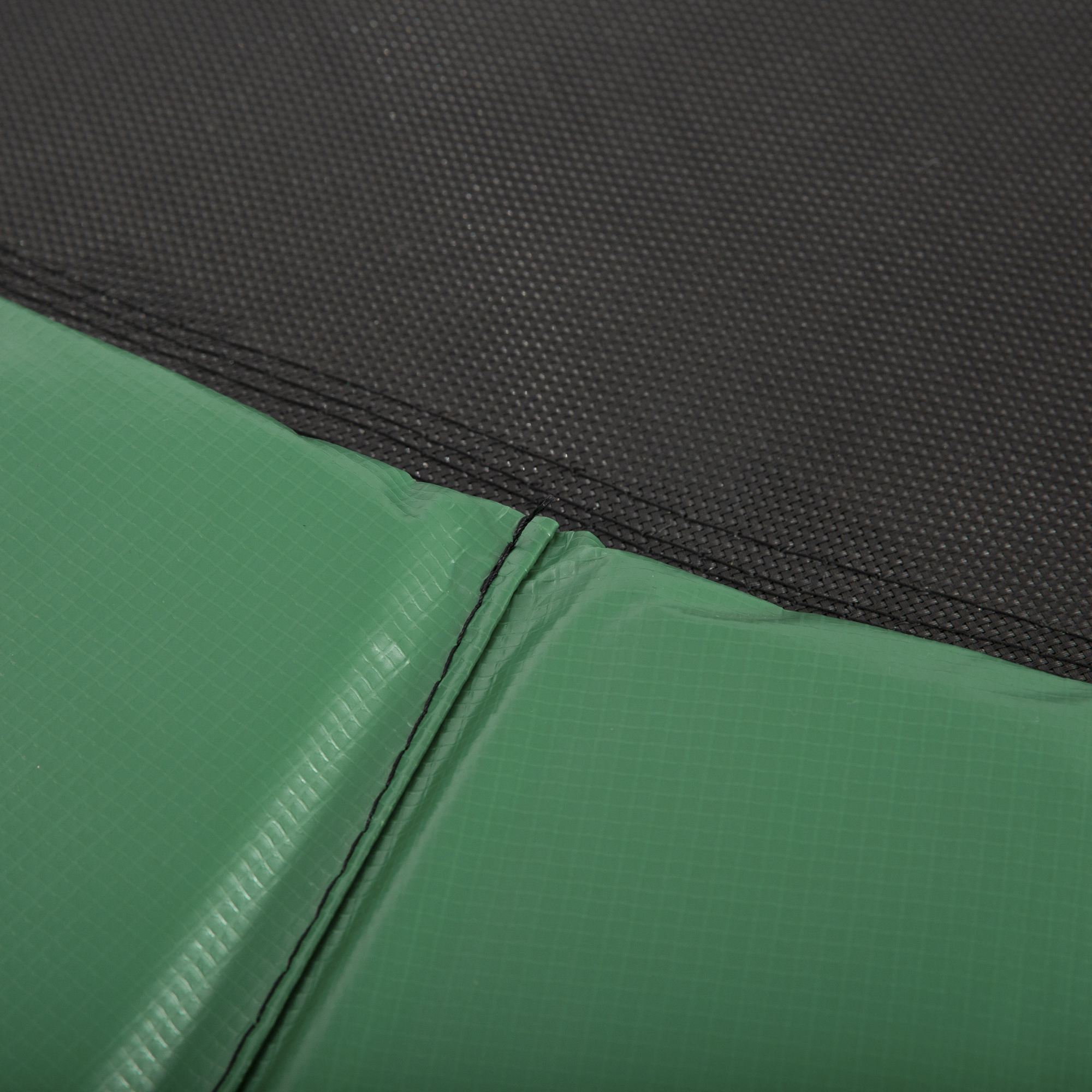 Un primer plano muestra la textura y las costuras de una almohadilla de seguridad verde para trampolín.