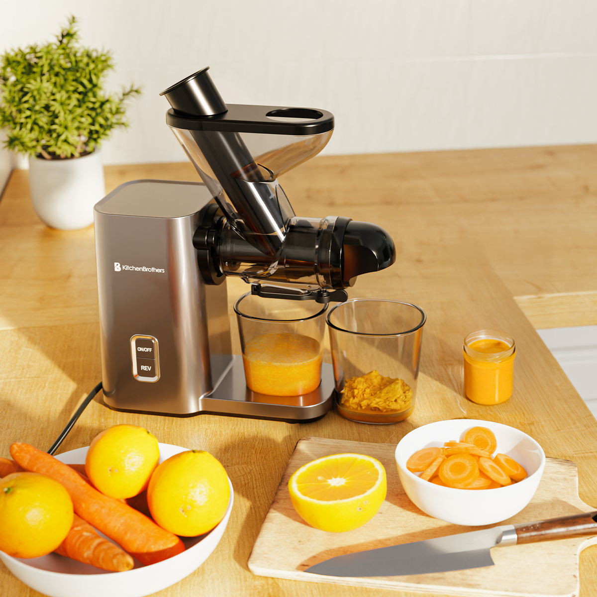 A silver juicer with cups of juice and pulp, surrounded by fruit on a wooden table.