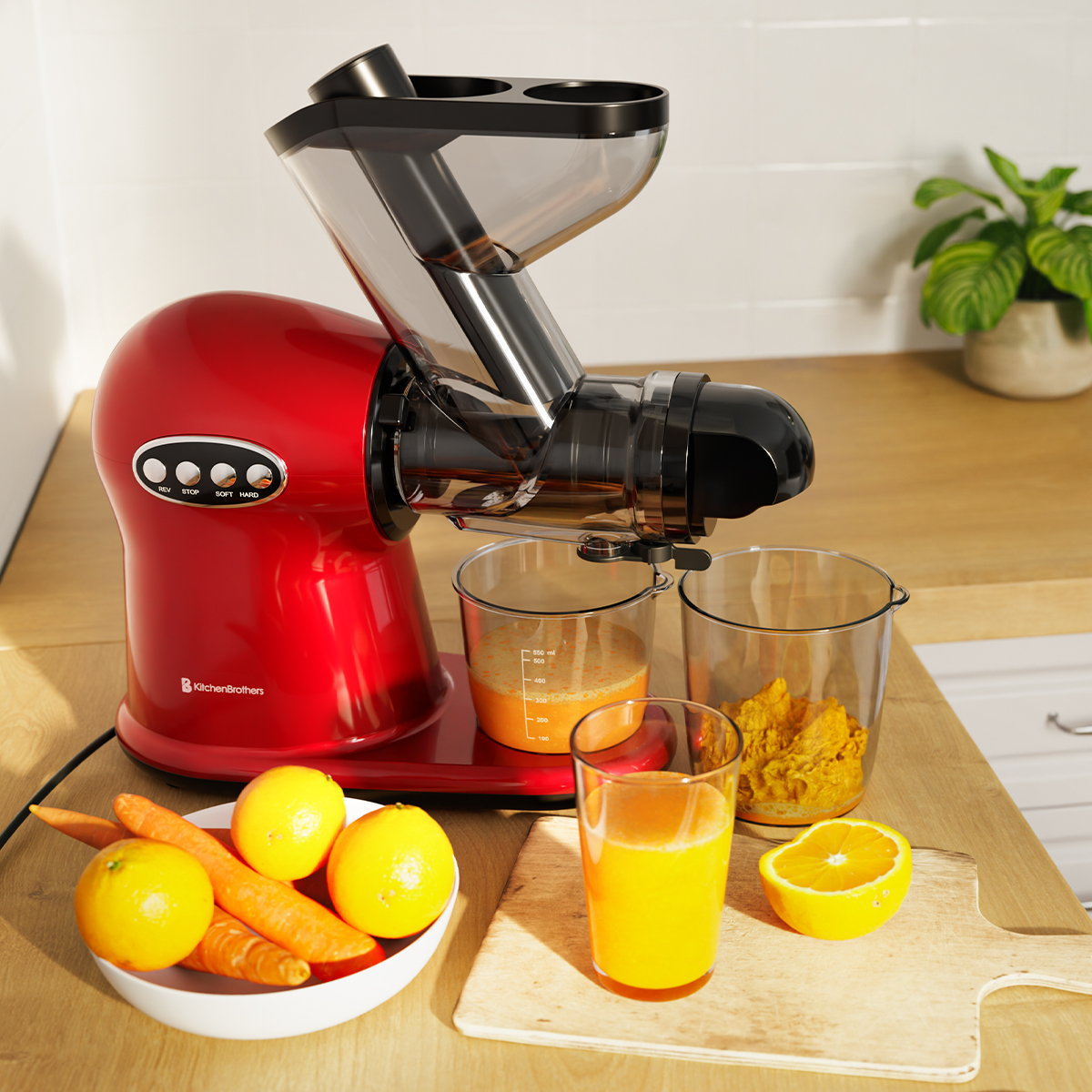 Rode KitchenBrothers slowjuicer die sinaasappelsap perst naast citroenen en wortelen.