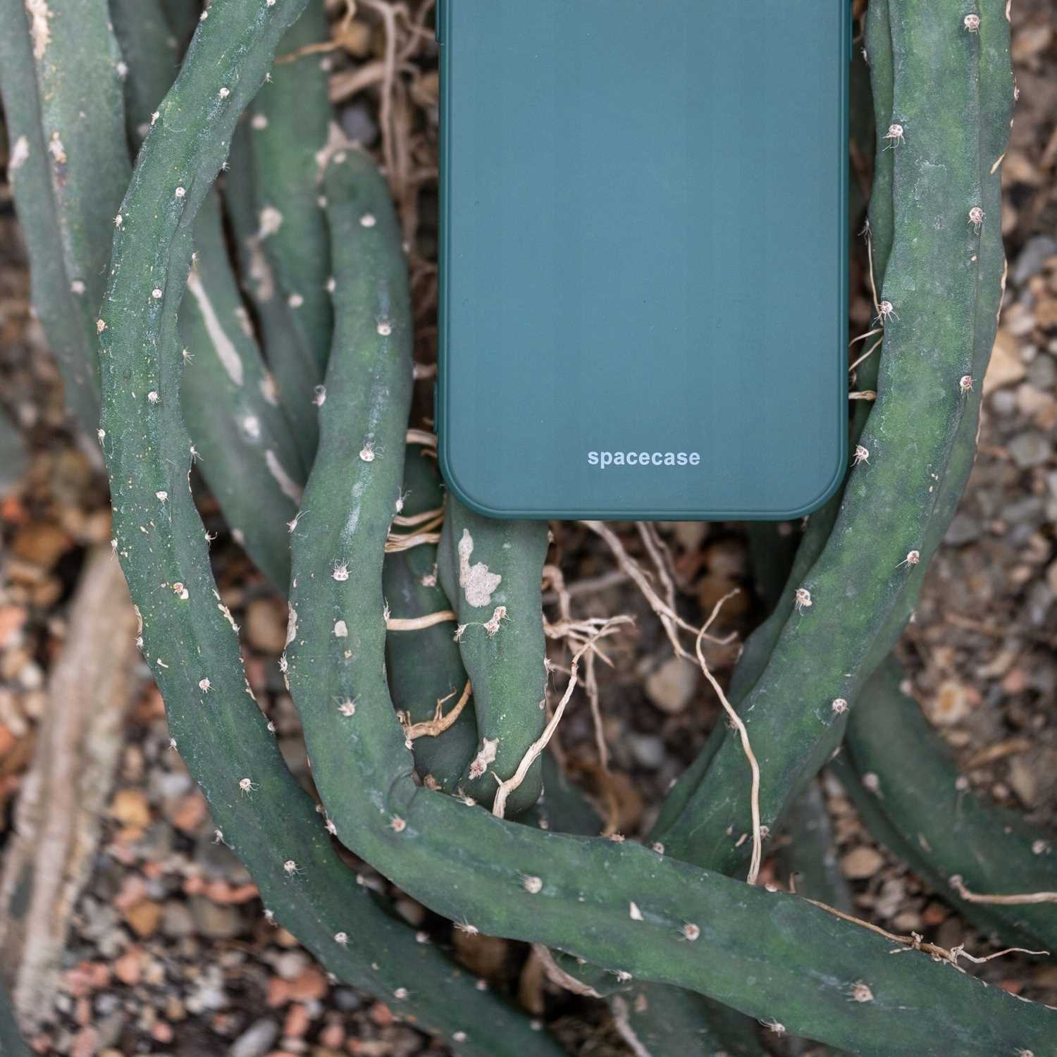 Ciemnozielone etui na telefon z logo 'spacecase' jest umieszczone na zielonych roślinach.