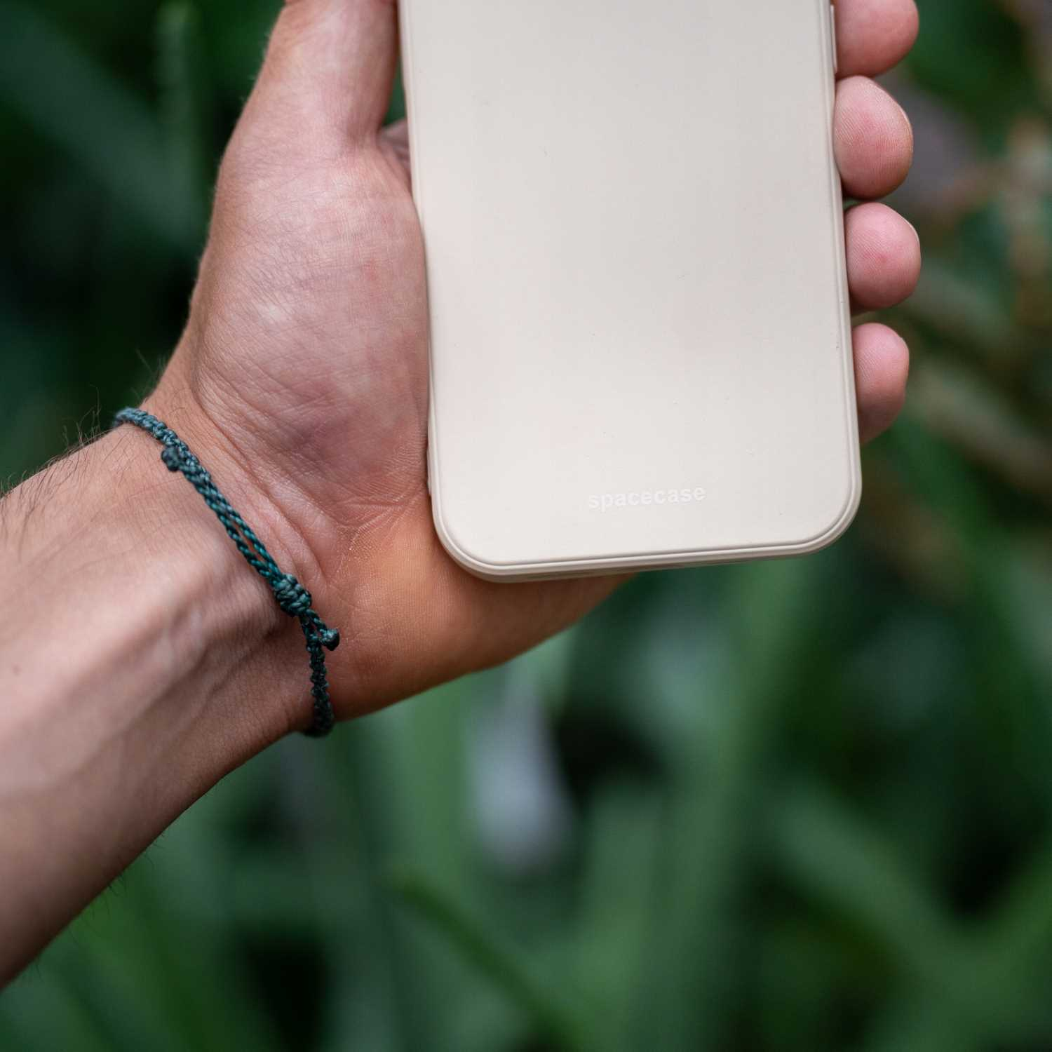 Ręka trzyma beżowe etui na telefon z logo 'spacecase', zielona bransoletka.